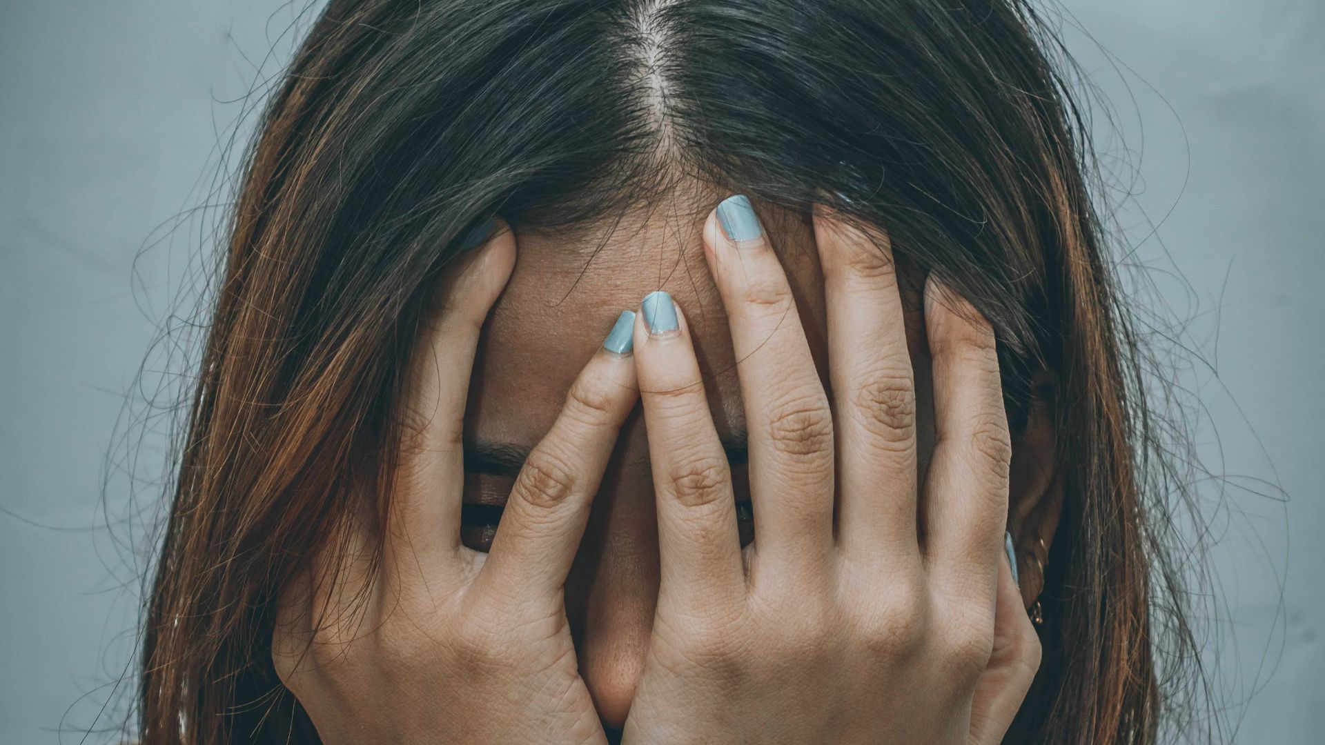 woman in brown sweater covering her face with her hand