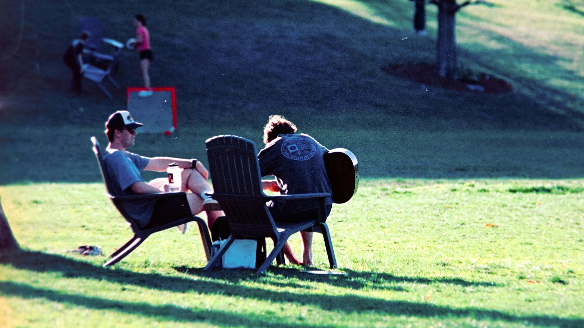 Two people relax on chairs in a sunny park.