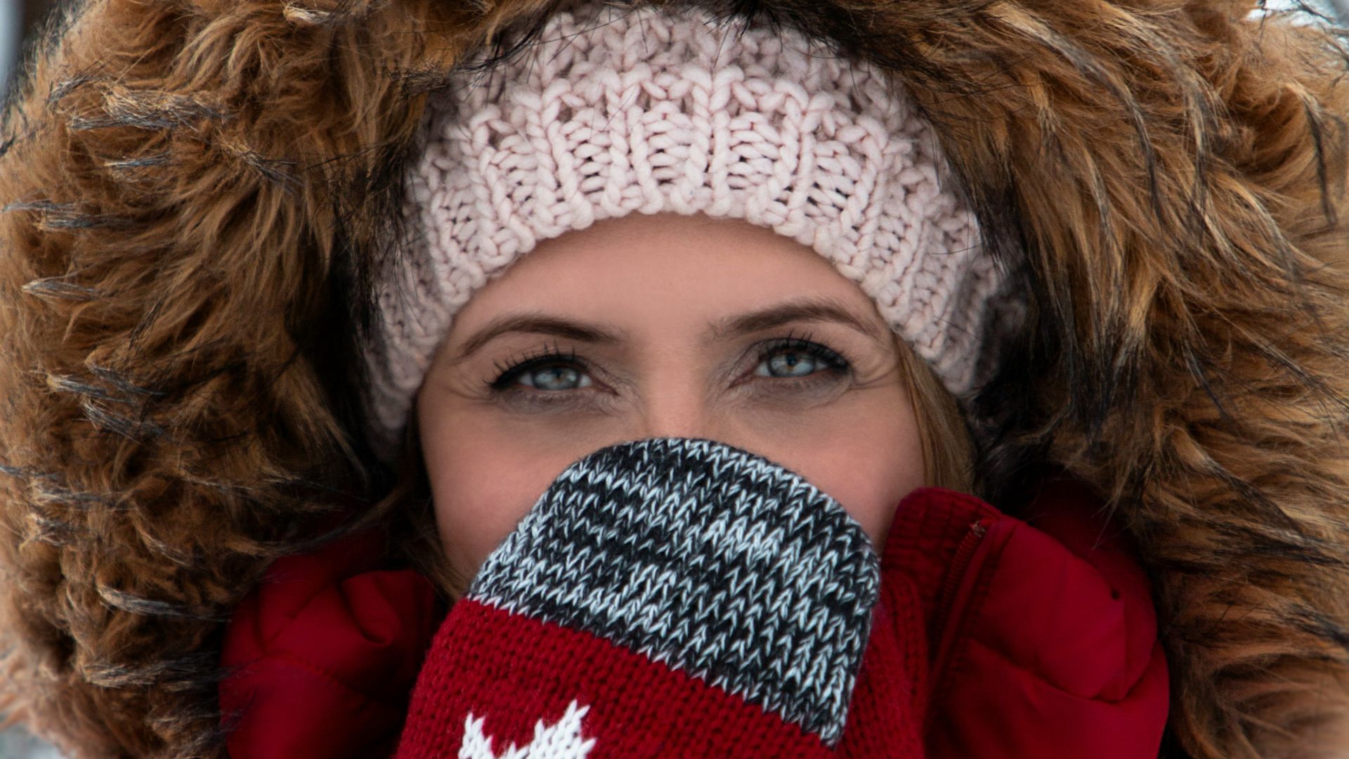 woman wearing red-and-brown parka coat and gray-and-red Canada knit mittens