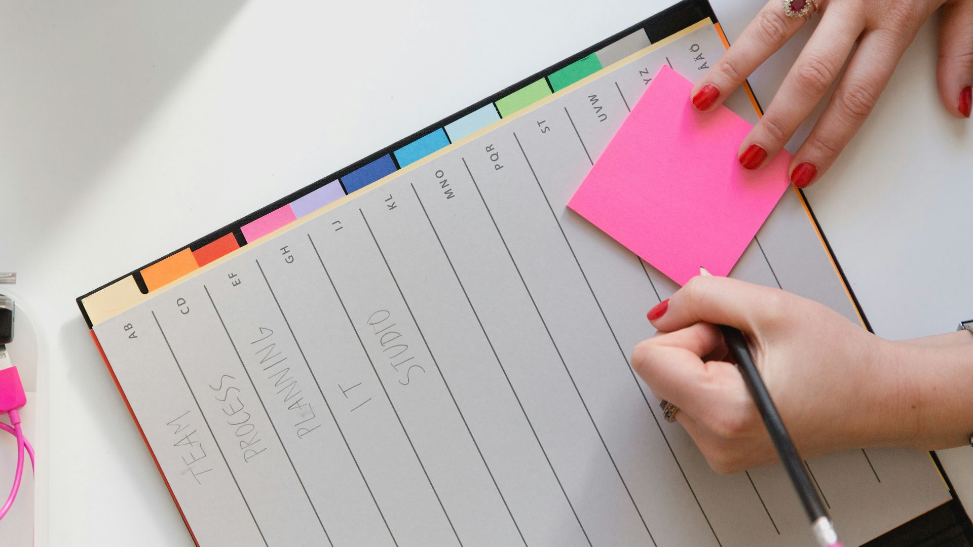 person holding pencil and stick note beside table