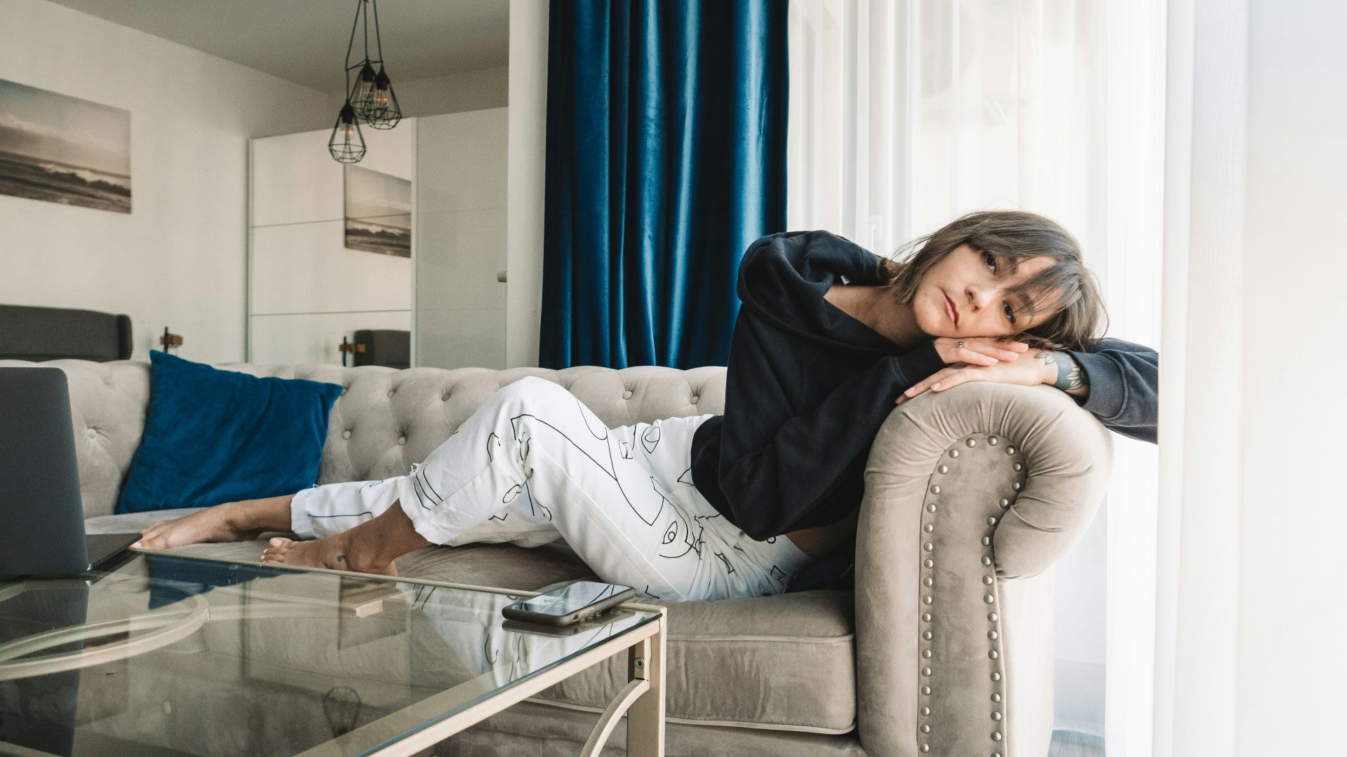 woman in gray sweater and blue denim jeans sitting on gray couch