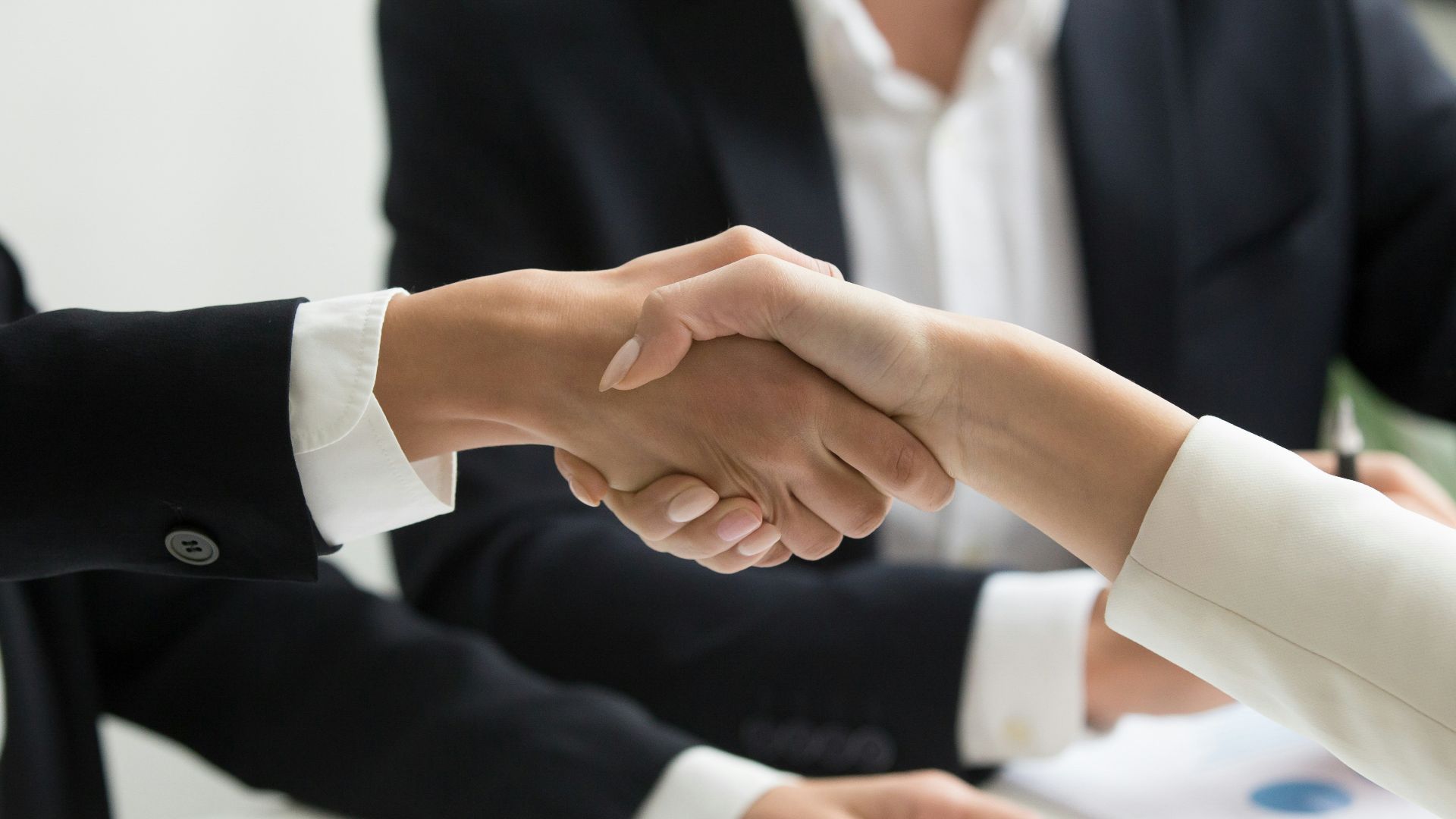 two people shaking hands in front of a laptop