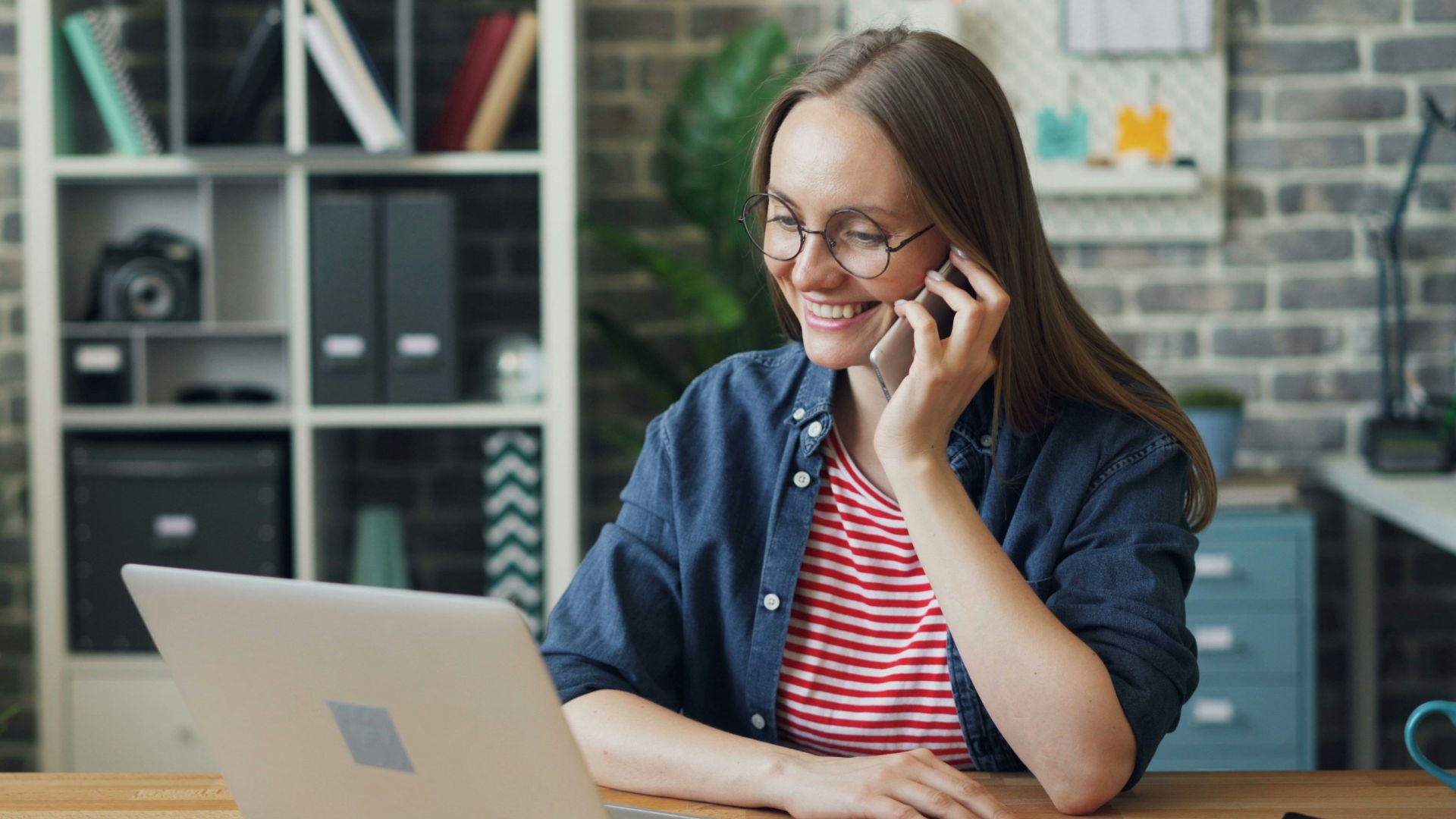 a woman talking on a cell phone while using a laptop