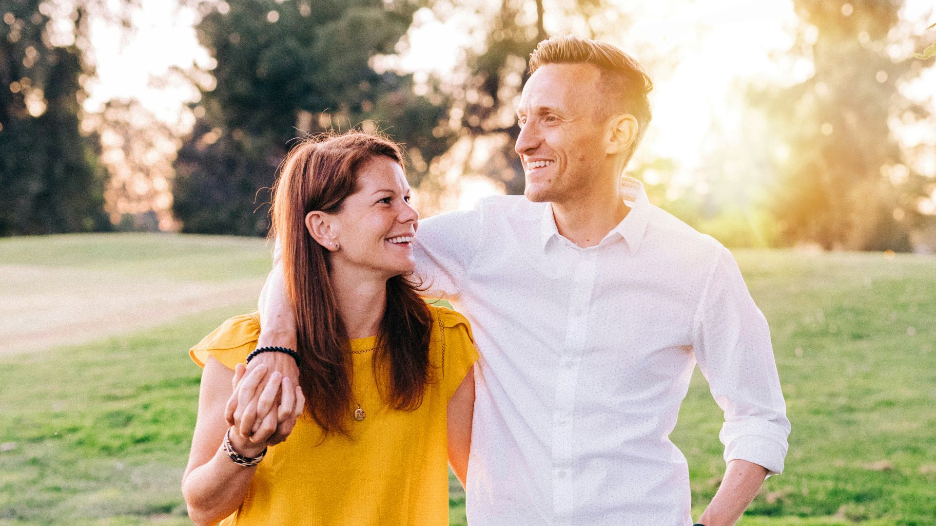 man in white dress shirt and woman in orange long sleeve shirt standing on green grass