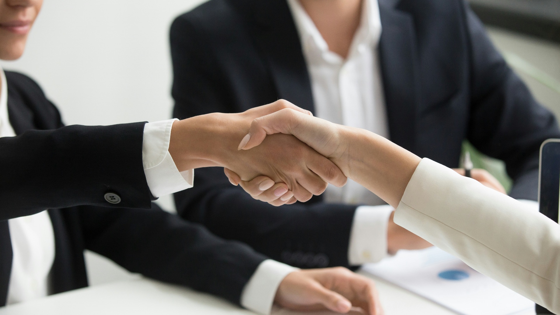 two people shaking hands in front of a laptop