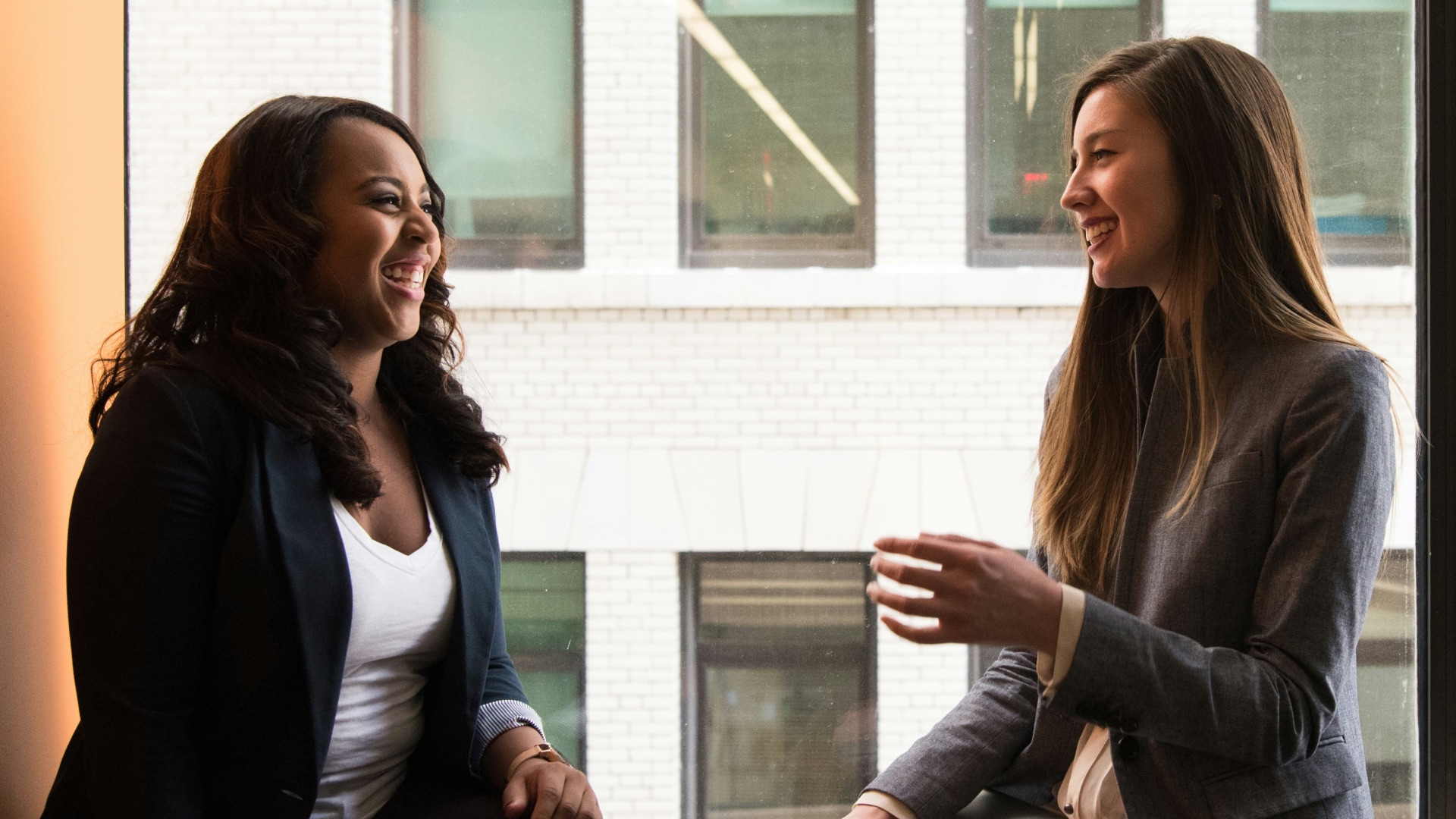 two woman sitting by the window laughing