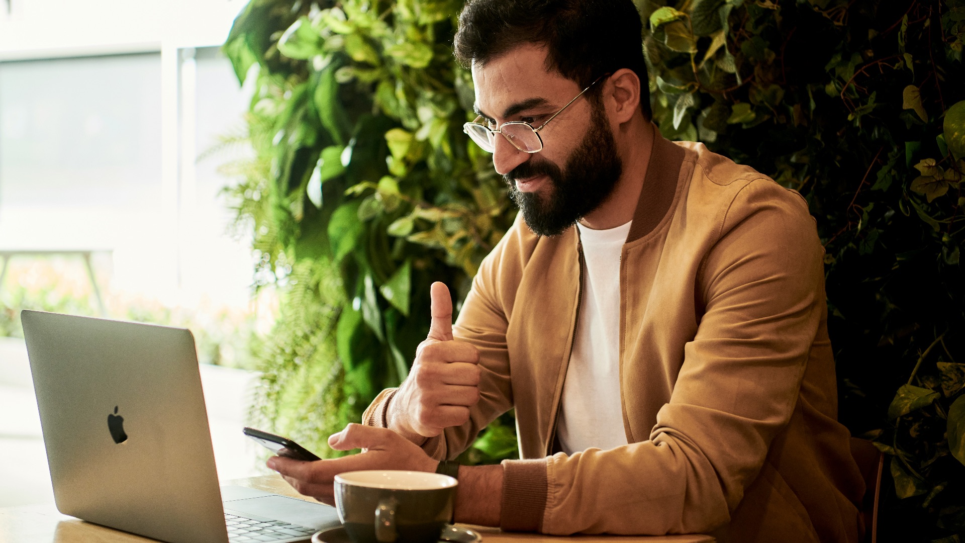 man in brown jacket sitting at a table looking at laptop