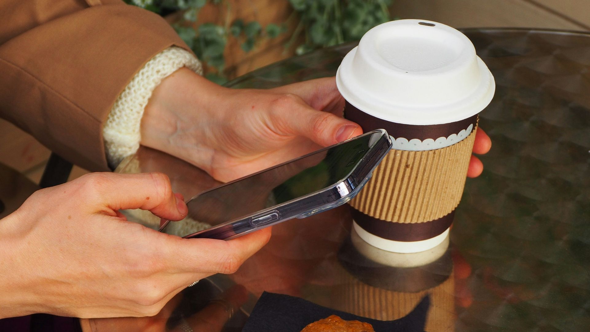 Person using phone with coffee and pastry on table