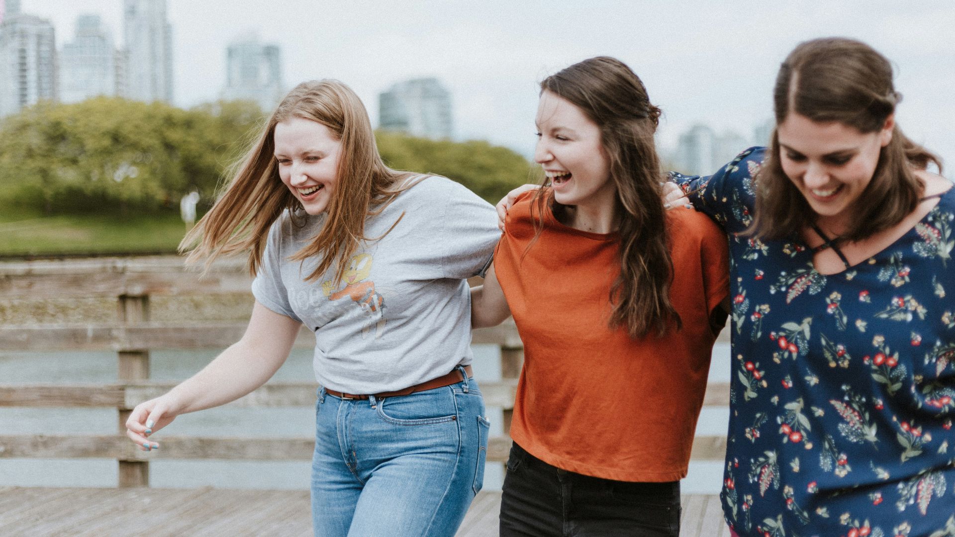 three women walking on brown wooden dock near high rise building during daytime