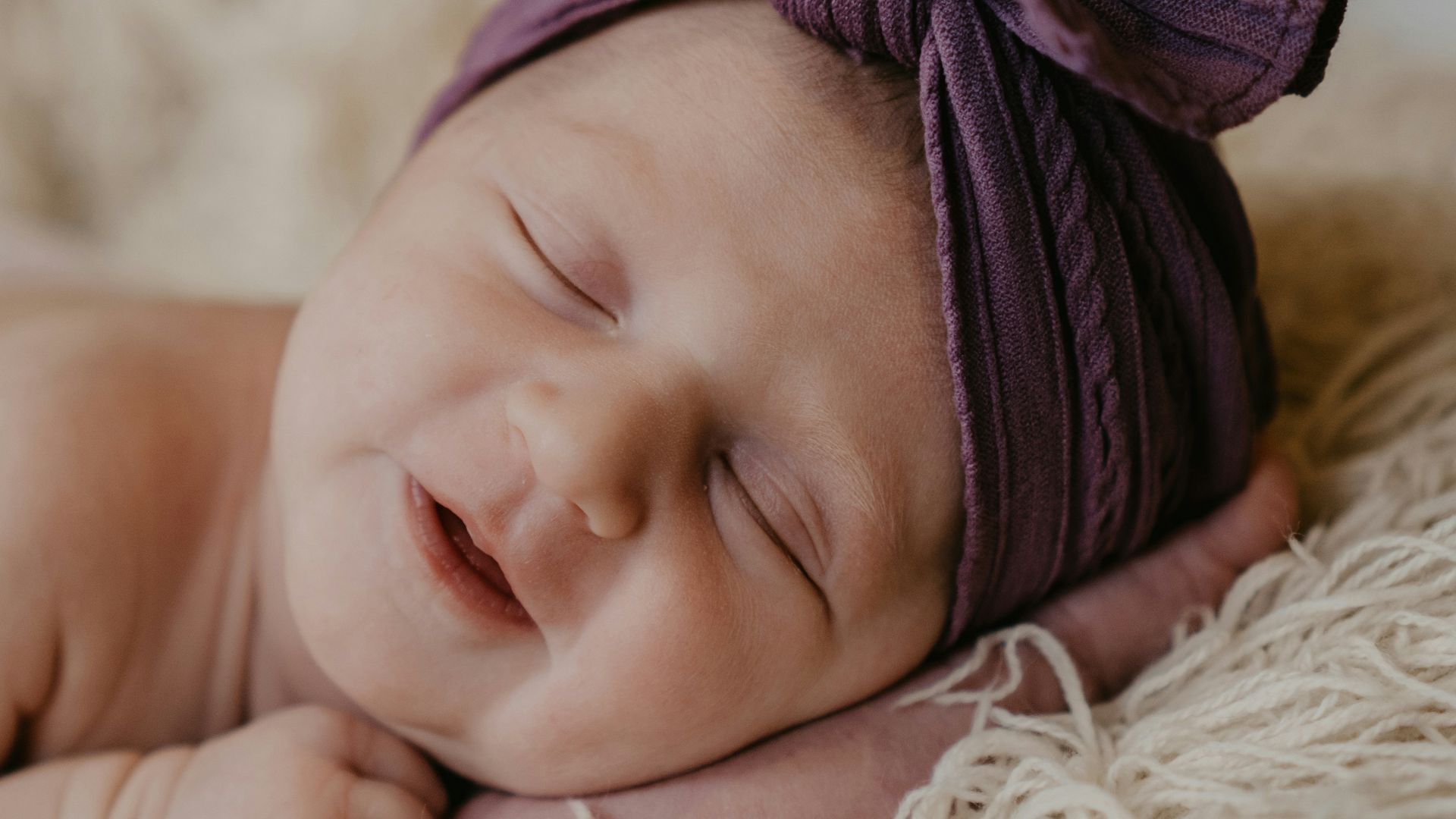 baby in purple knit cap lying on white fur textile