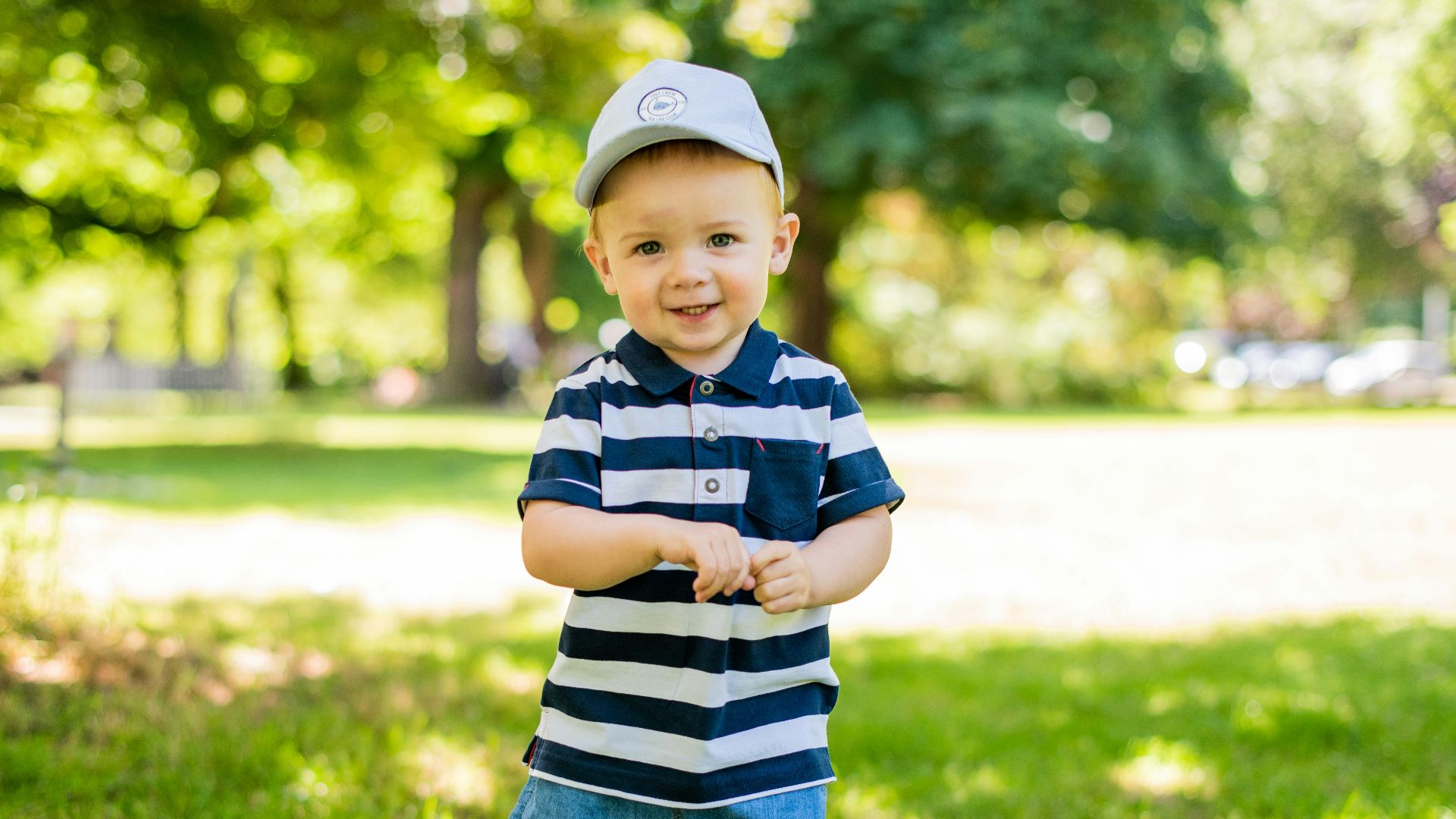 boy in black and white stripe polo shirt and blue denim shorts standing on green grass