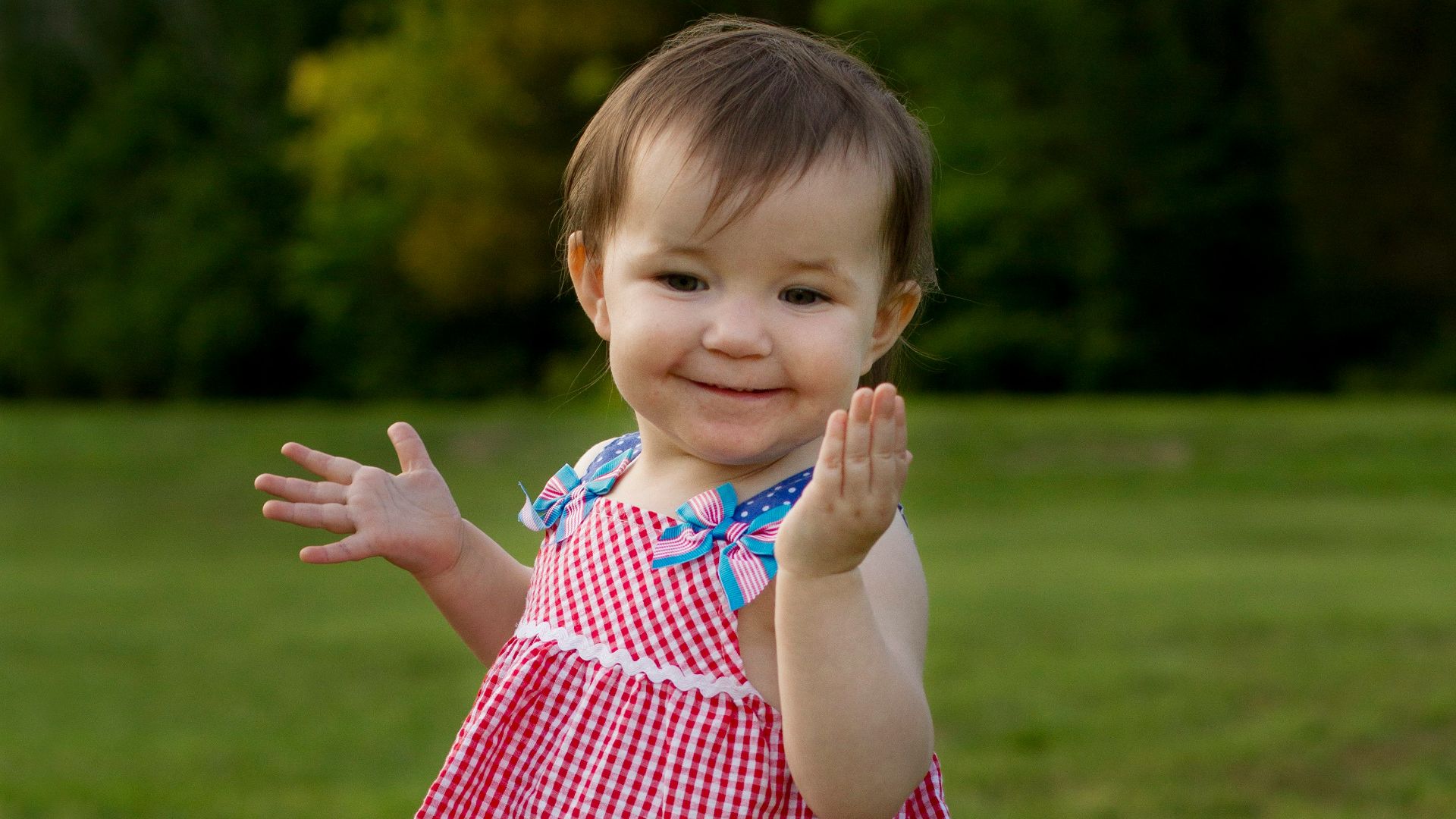 a little girl in a red and blue dress standing in the grass