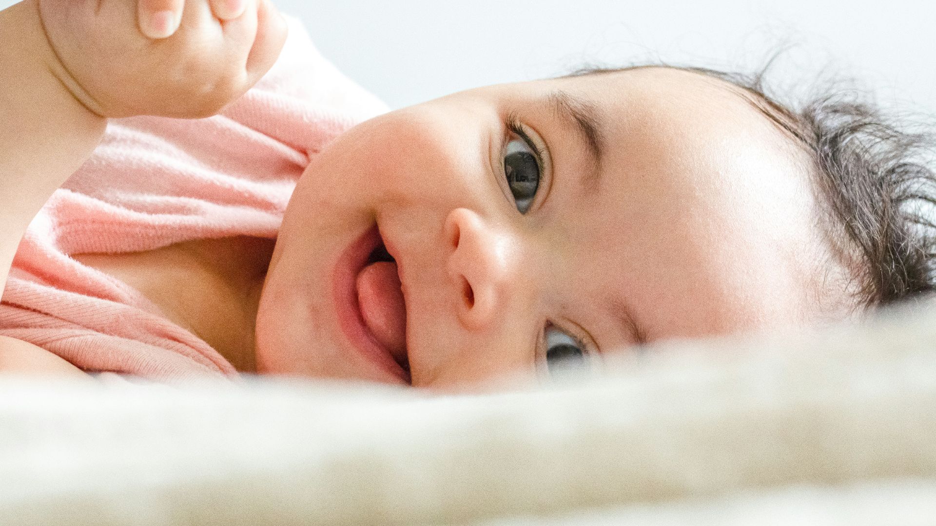 baby in pink shirt lying on white textile