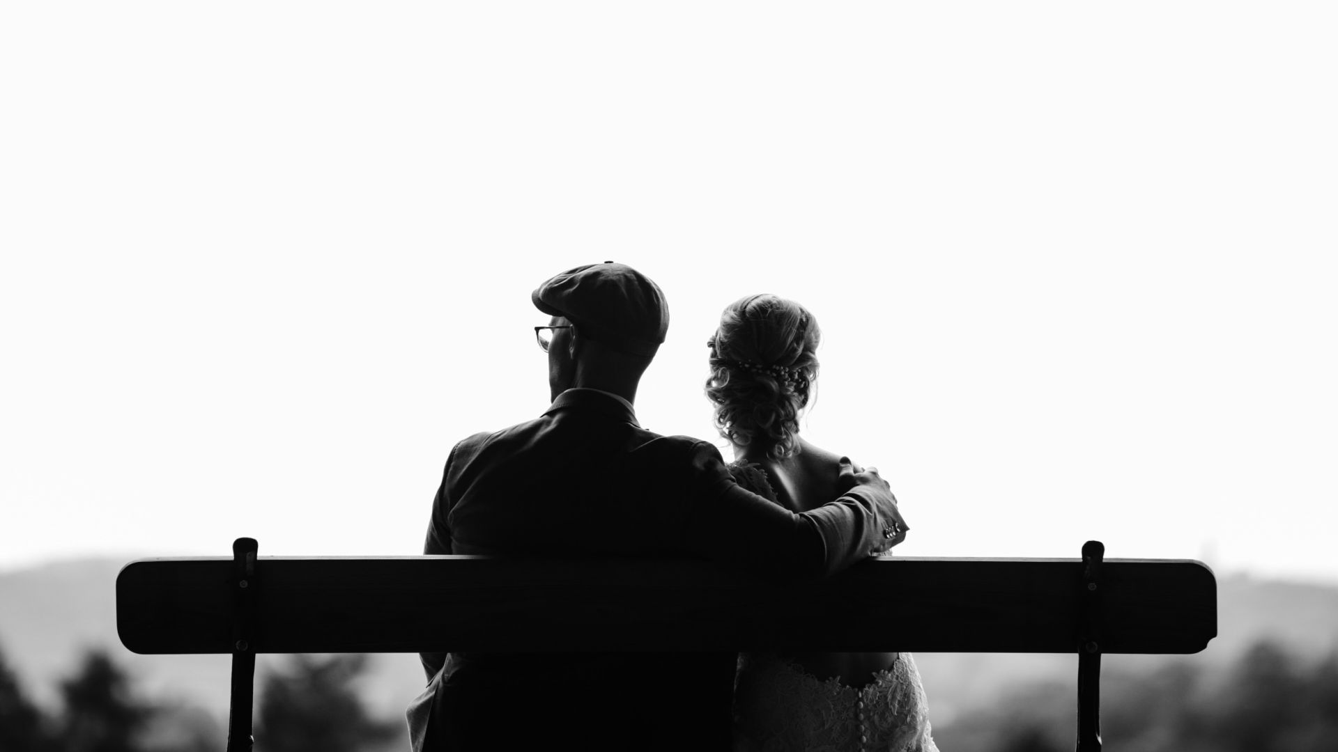 couple sitting on bench under tree grayscale photography
