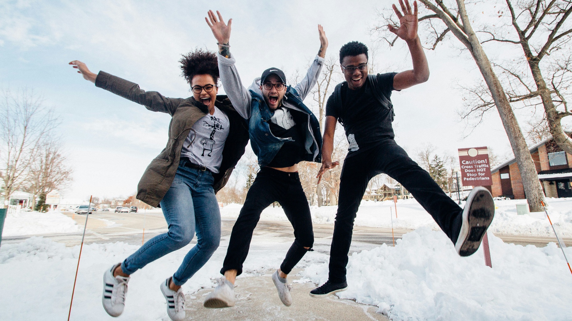 photo of three men jumping on ground near bare trees during daytime