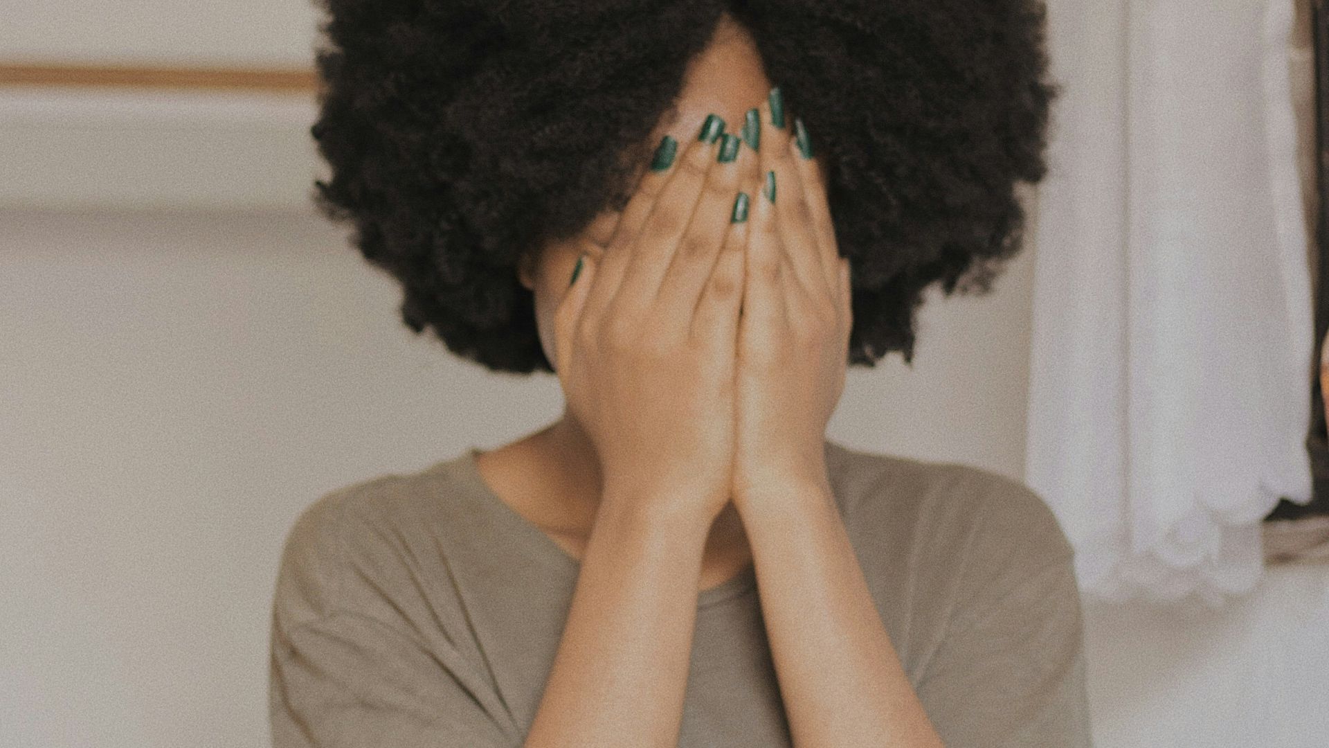 woman in gray t-shirt covering face with both hands