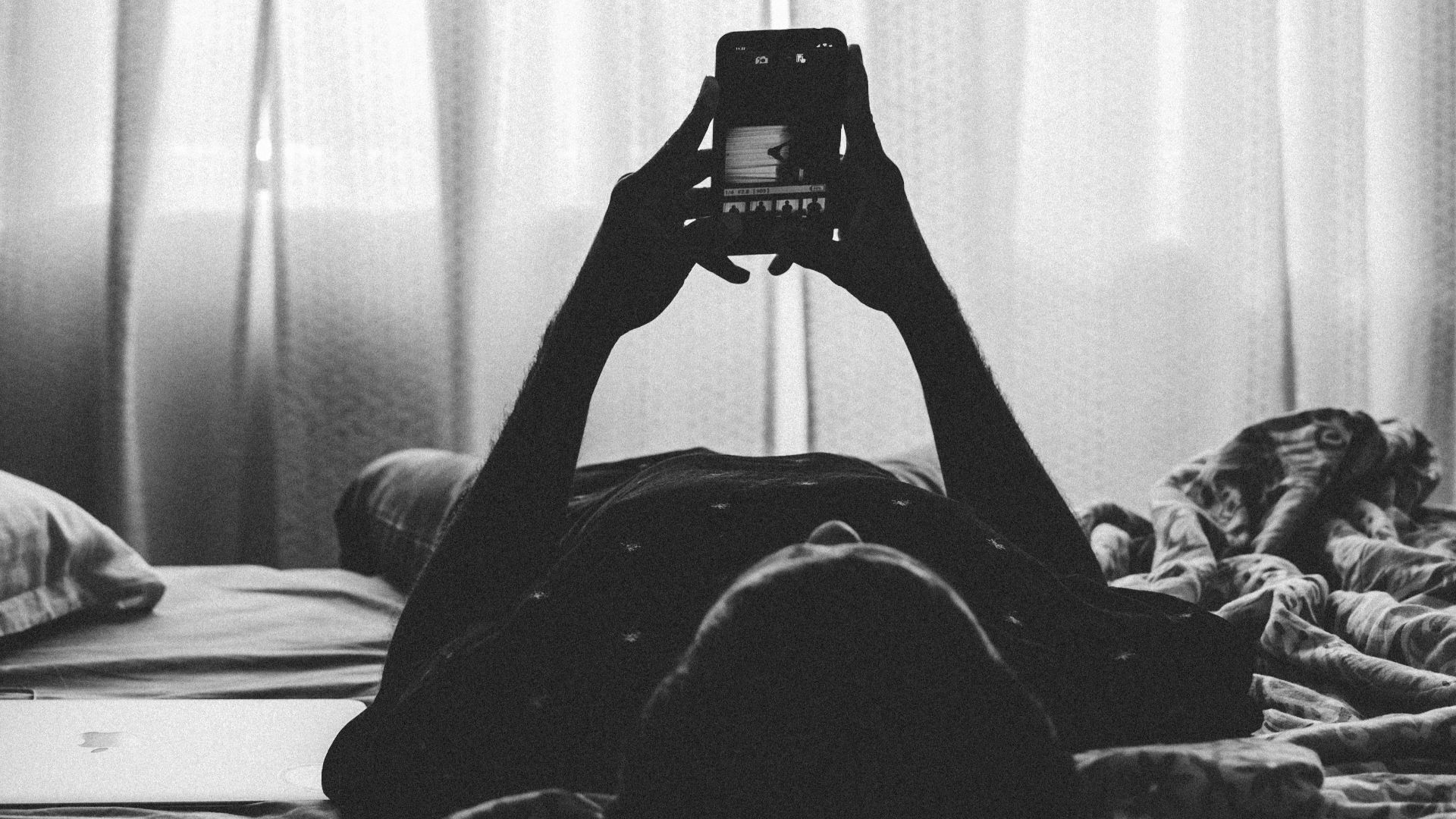 man lying on bed using smartphone