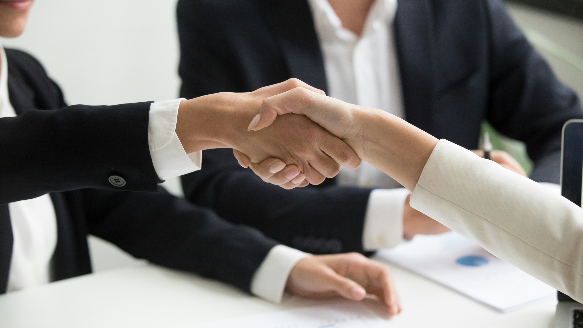 two people shaking hands in front of a laptop