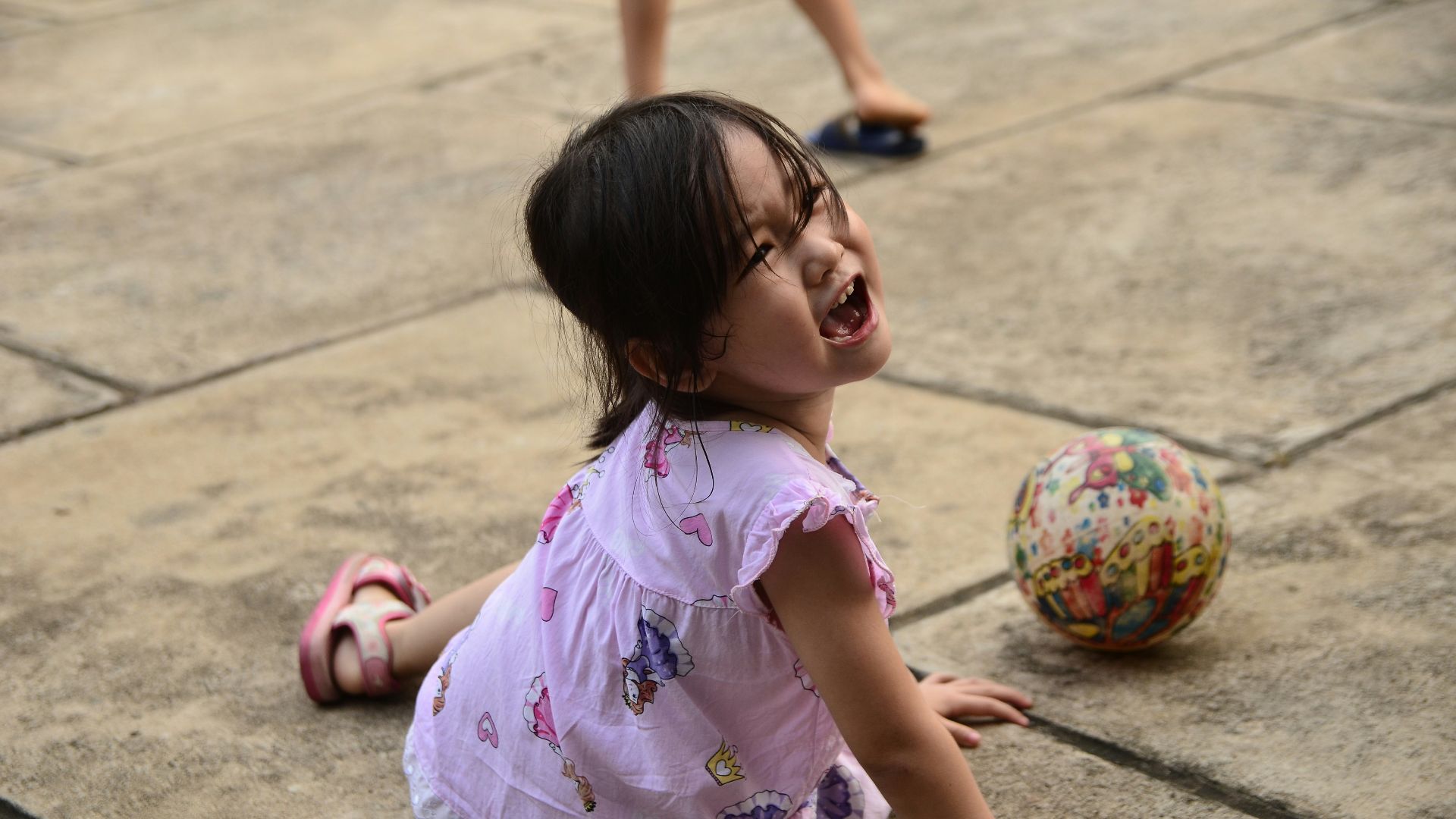 girl in pink and white floral dress sitting on gray concrete floor during daytime