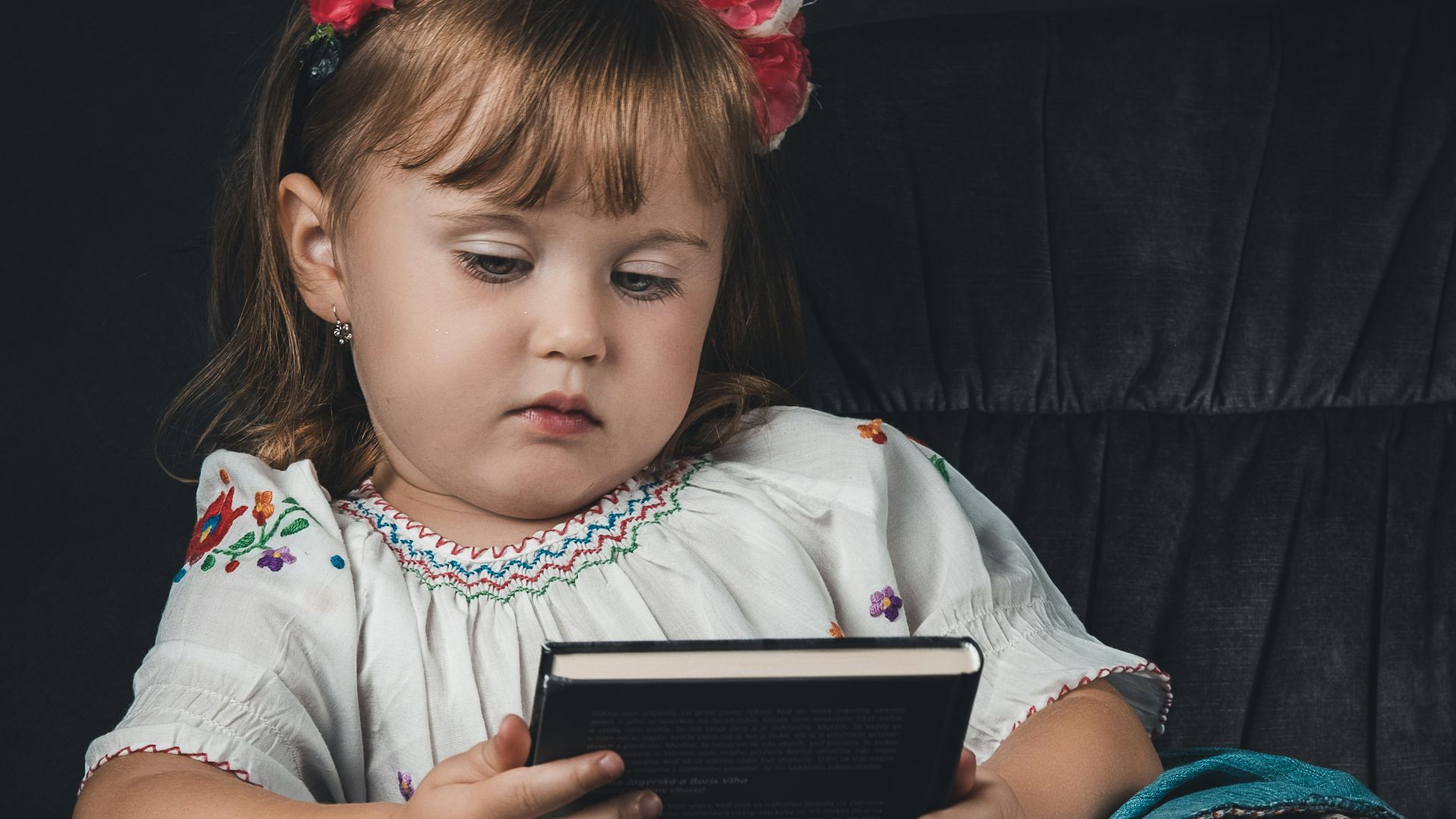 a little girl sitting in a chair reading a book