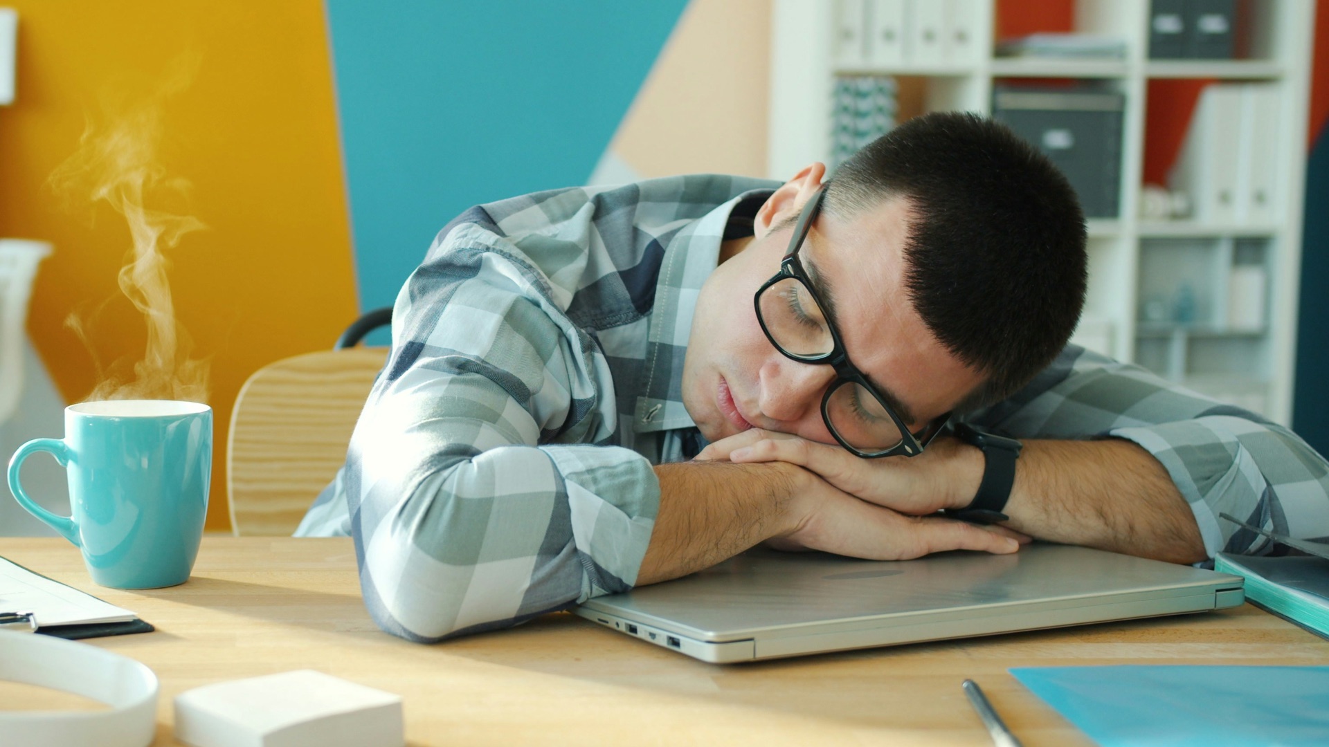Man sleeping at desk with coffee and laptop.