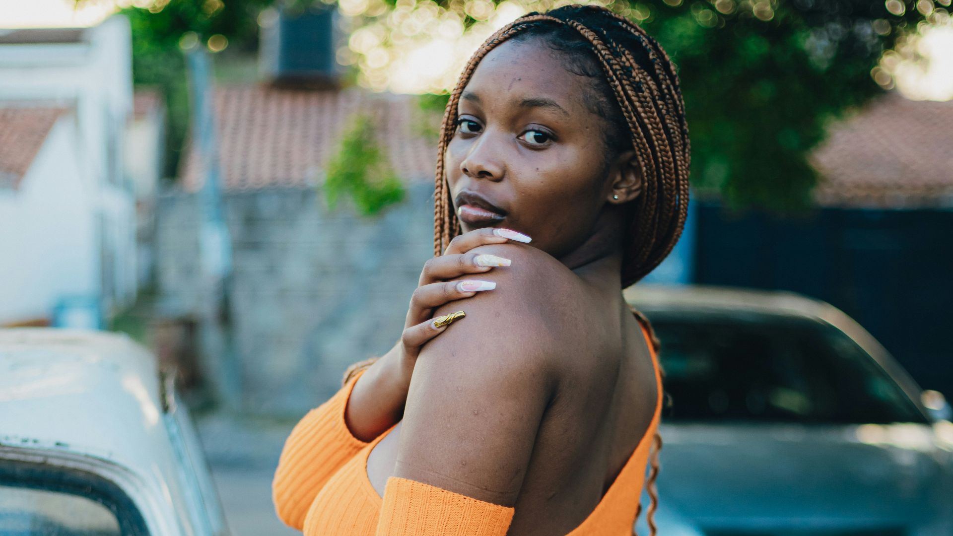 A woman in an orange dress poses by a car.