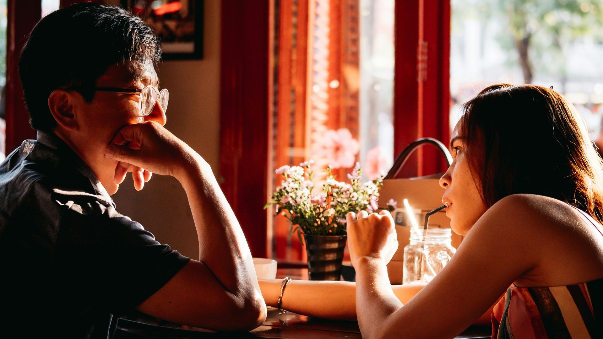 man wearing black collared top sitting on chair in front of table and woman wearing multicolored top