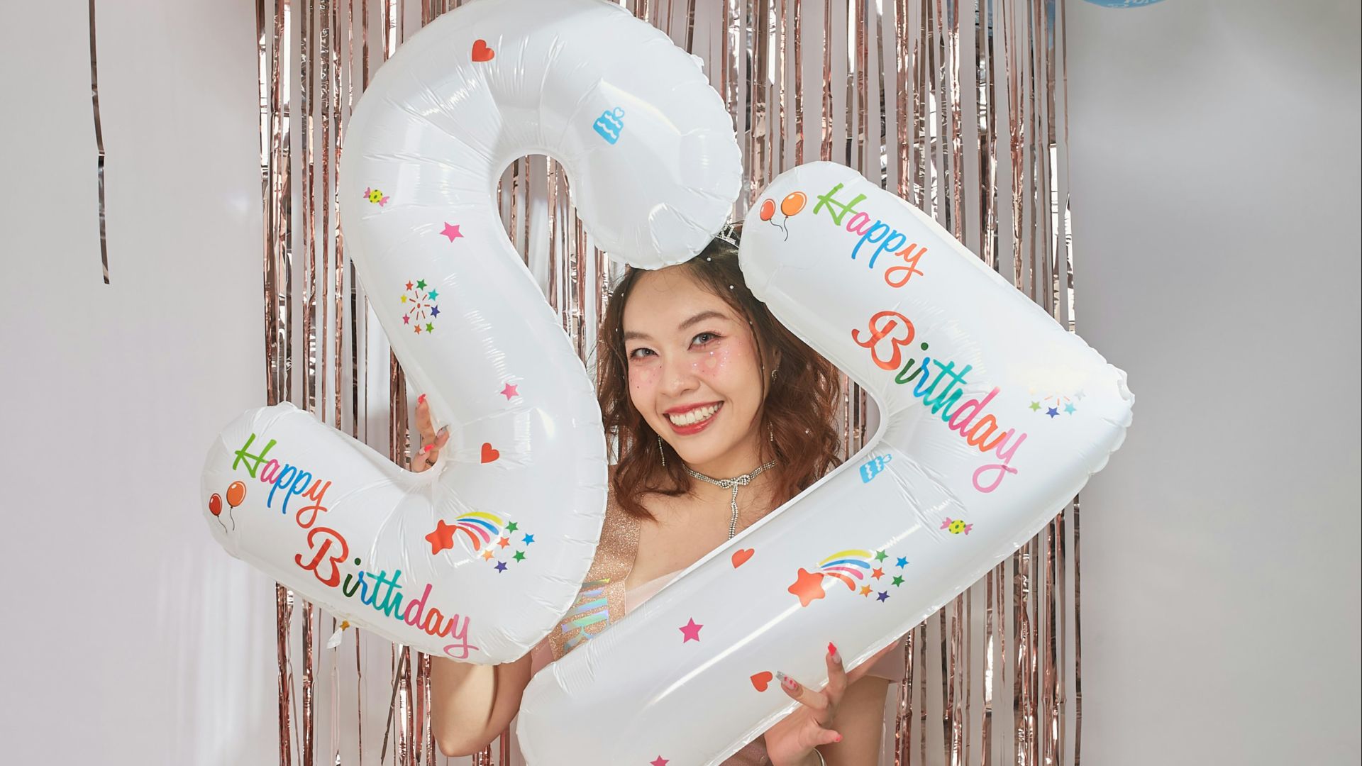 A woman holding a large number balloon in front of a birthday banner