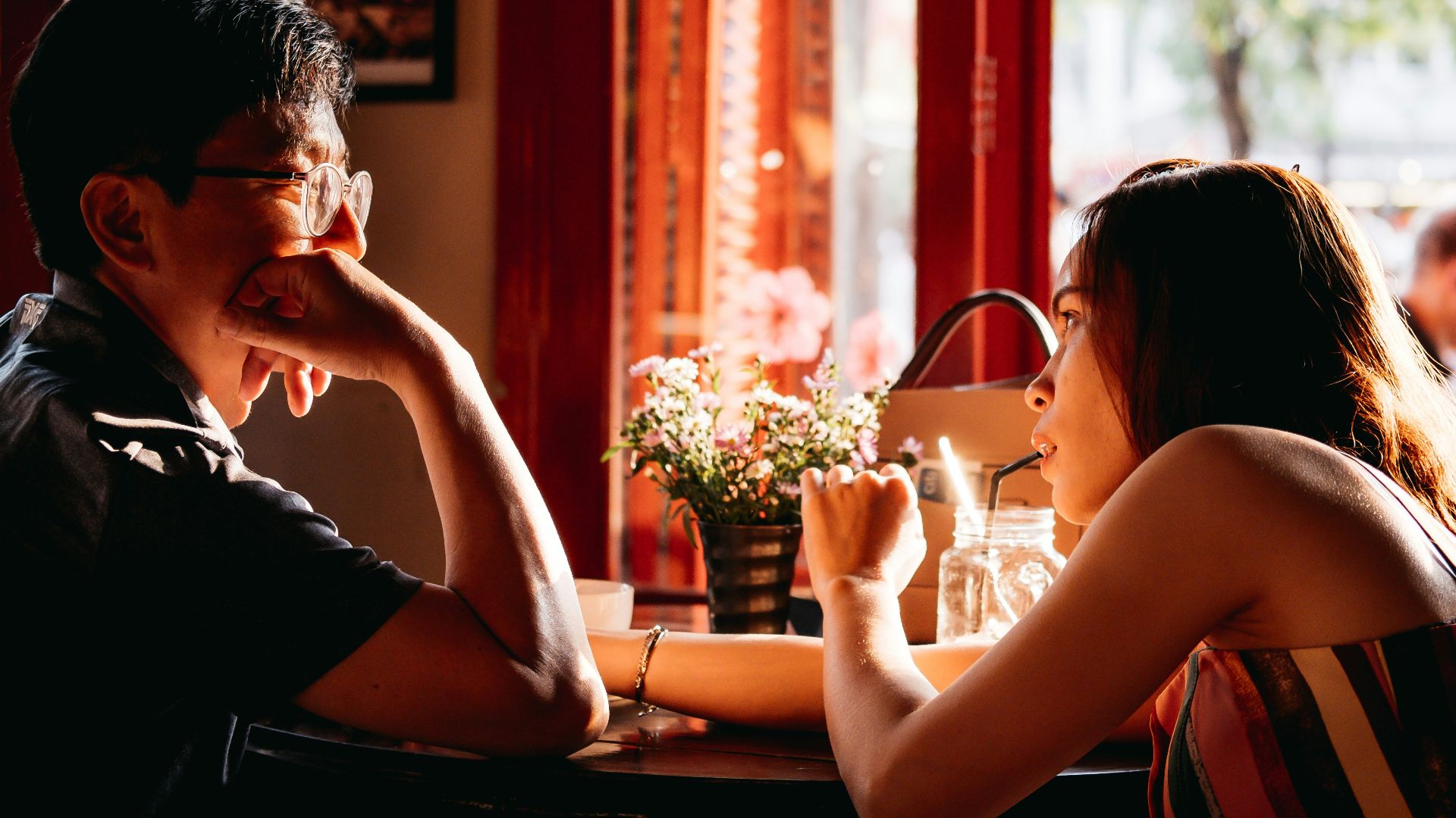 man wearing black collared top sitting on chair in front of table and woman wearing multicolored top