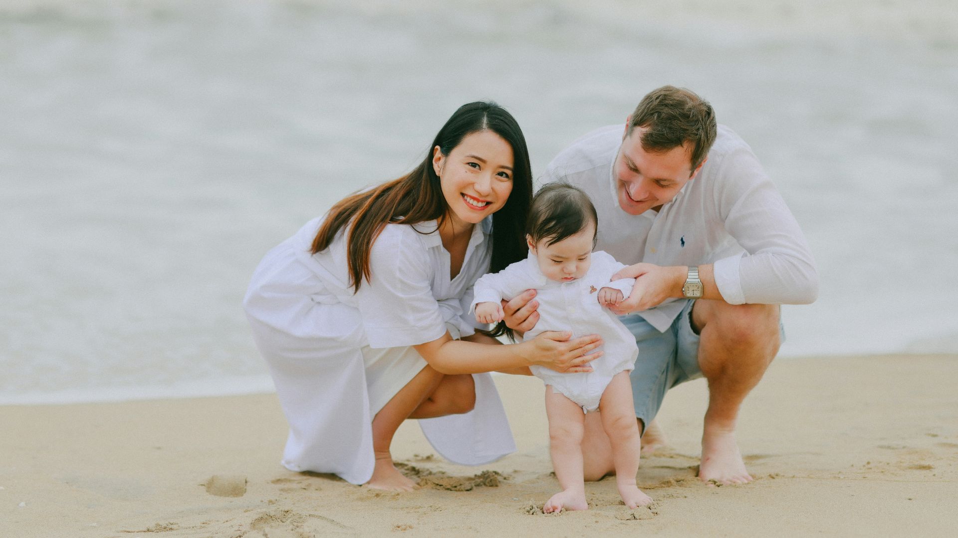 Family posing on a sandy beach near the ocean.