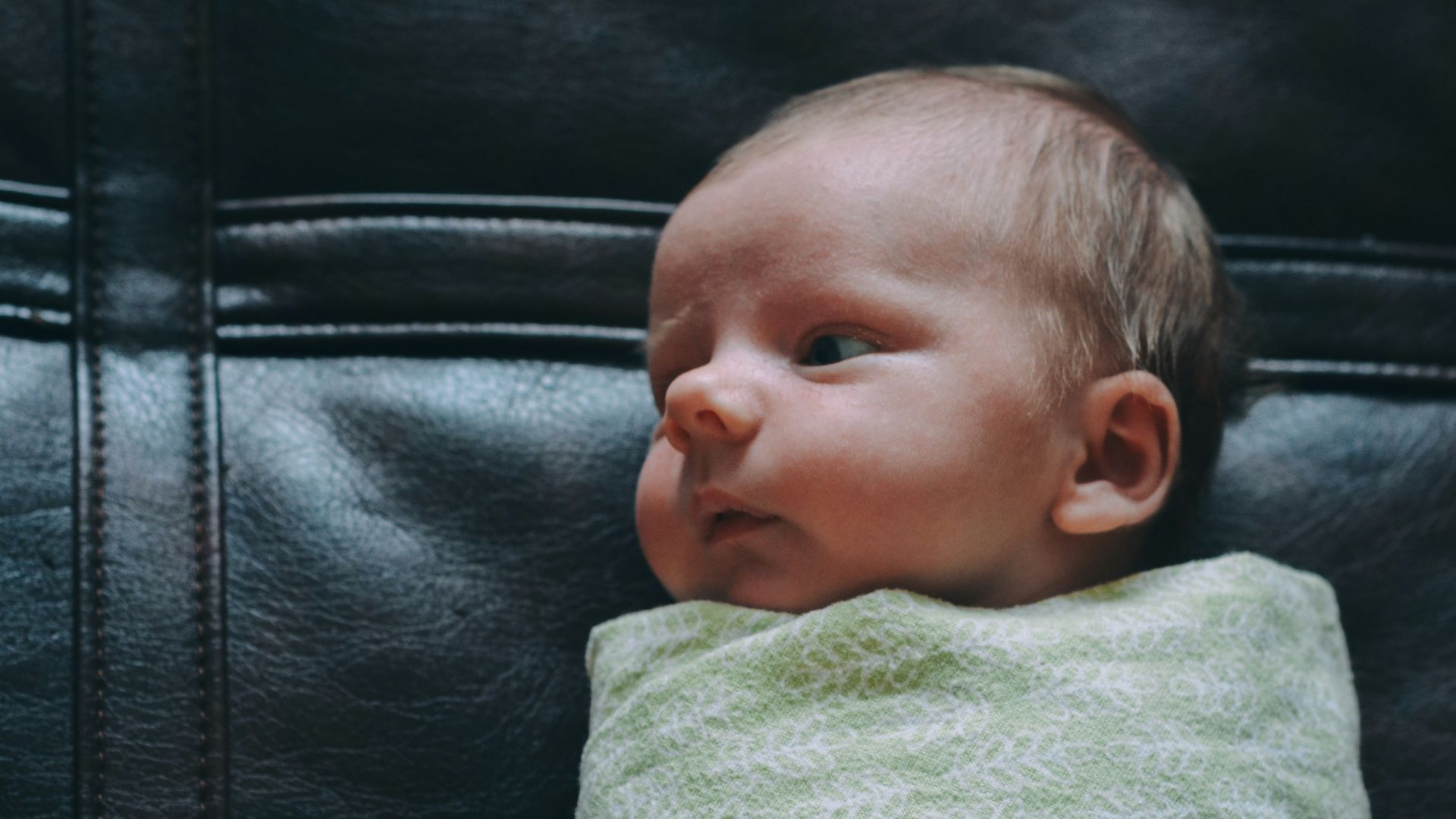 baby covered in green blanket on black leather surface