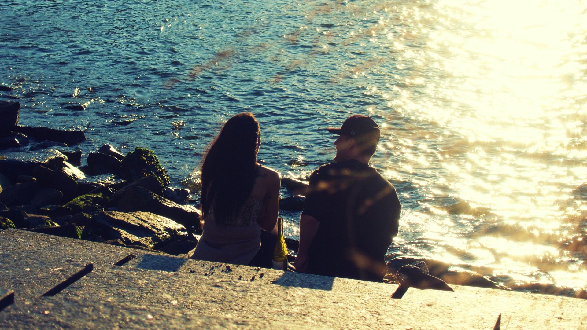 silhouette of people sitting on rock near body of water during daytime