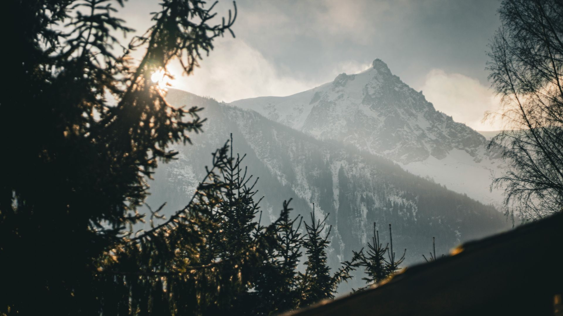 The sun shines through the clouds over a mountain