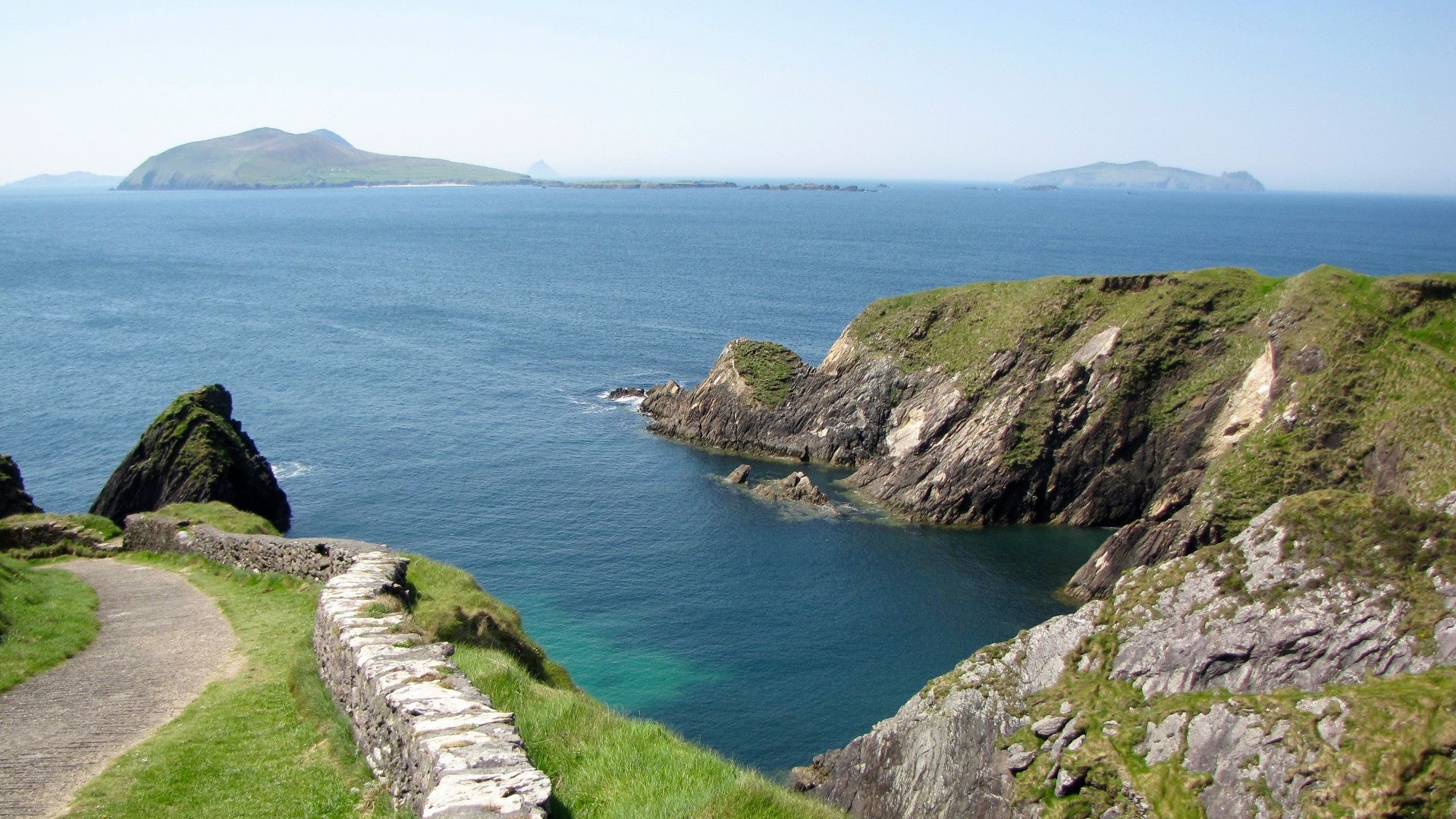 Coastal cliff path overlooking a calm blue bay.