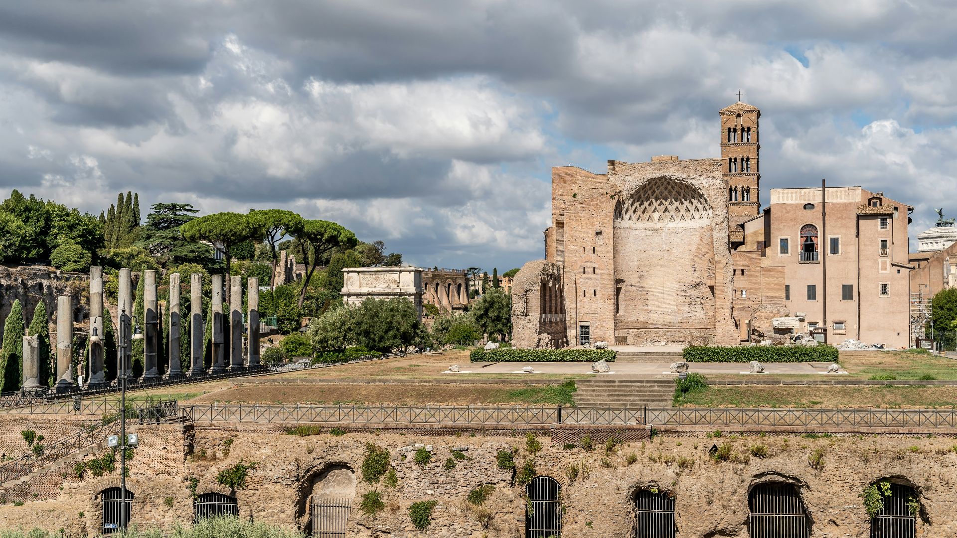 a stone building with a stone wall with Roman Forum in the background