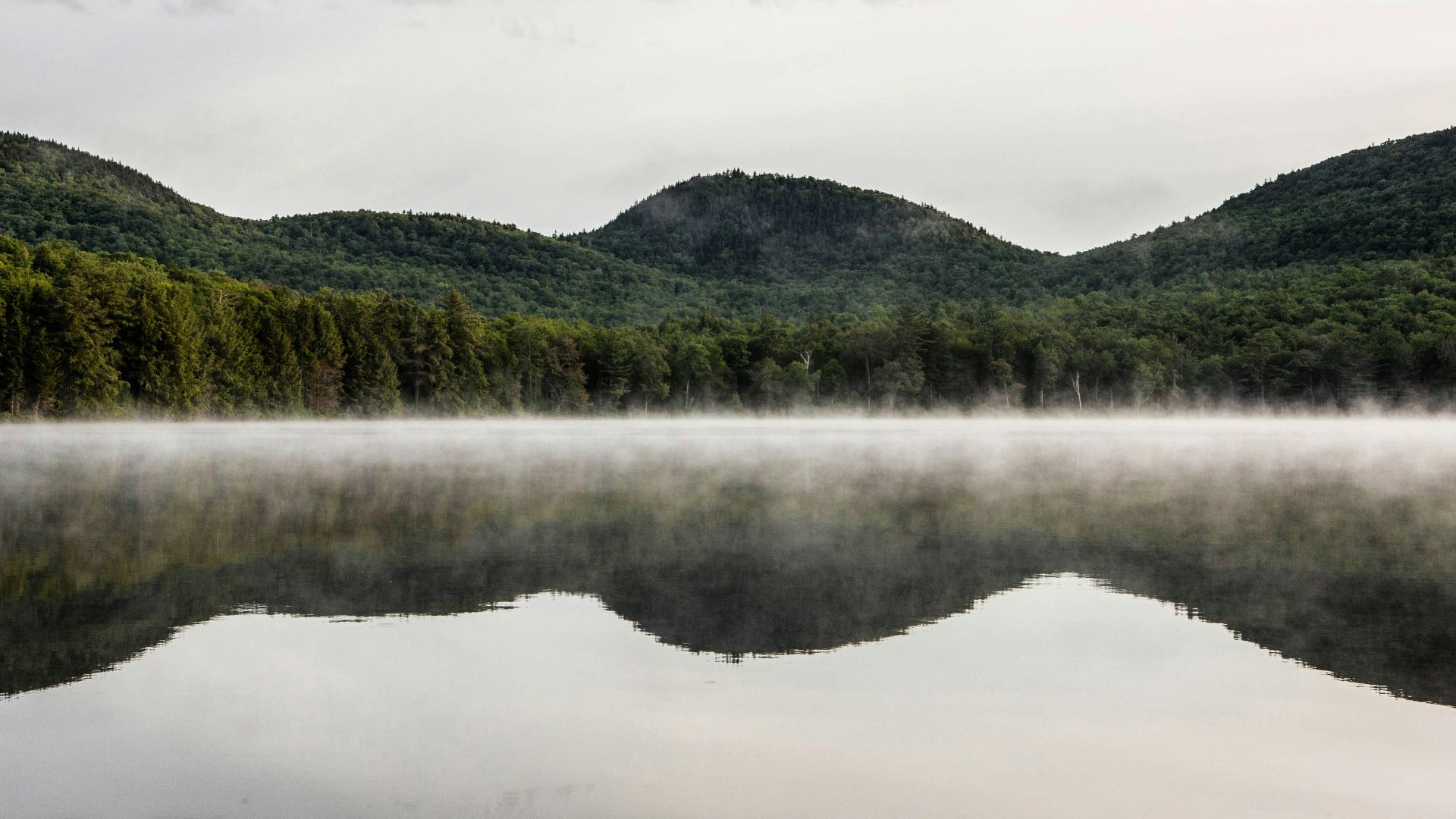 green mountain beside body of water under cloudy sky during daytime
