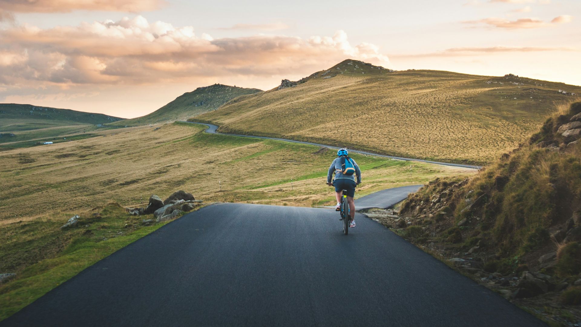 person cycling on road distance with mountain during daytime