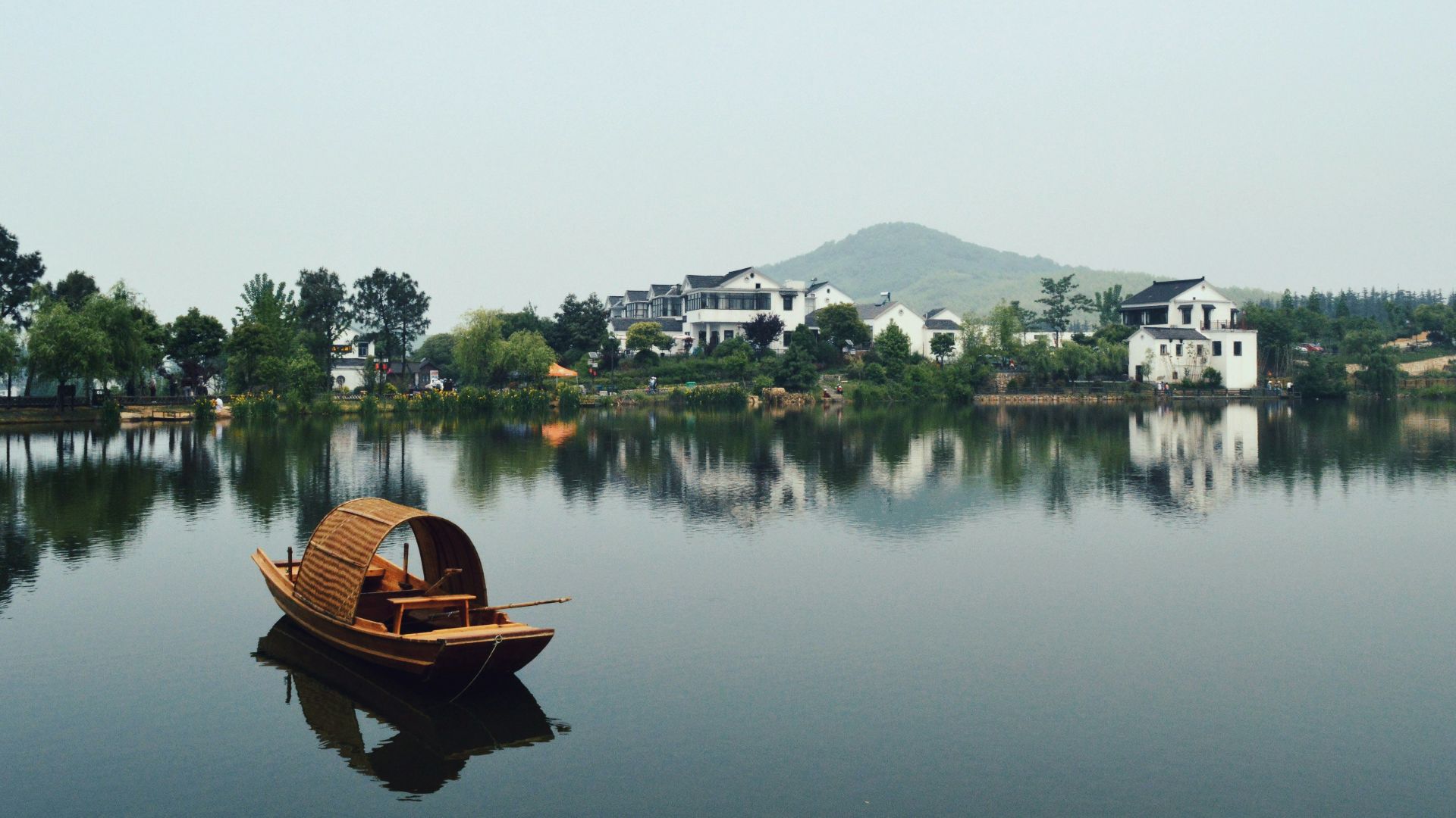 brown wooden boat on body of water overlooking houses by the shore at daytime