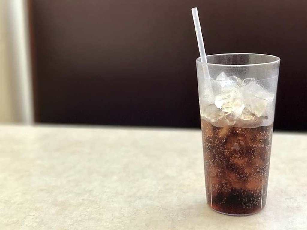 resizeclear-plastic-drinking-cup-half-filled-with-black-liquid-and-ice-on-white-wooden-table.jpg.optimal.jpg