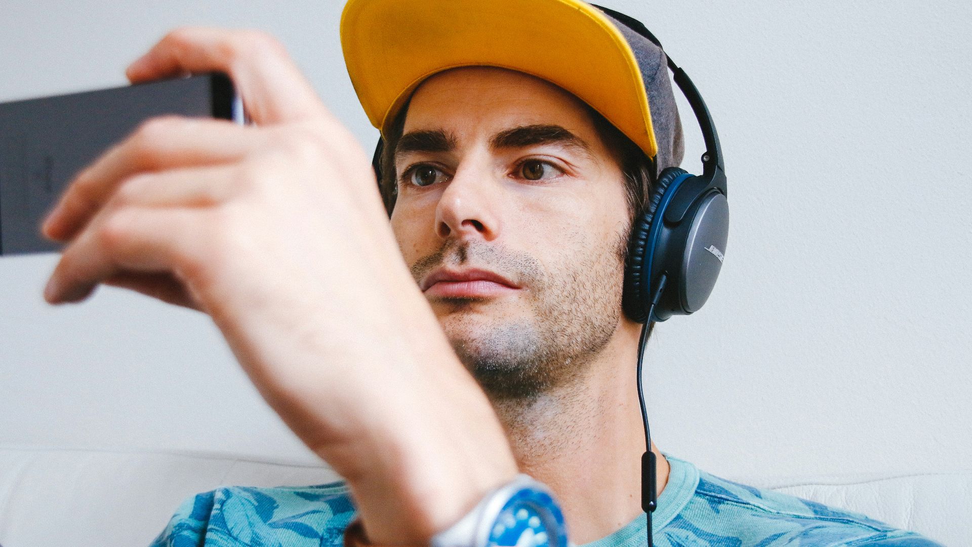 man wearing black corded headphones while holding phone