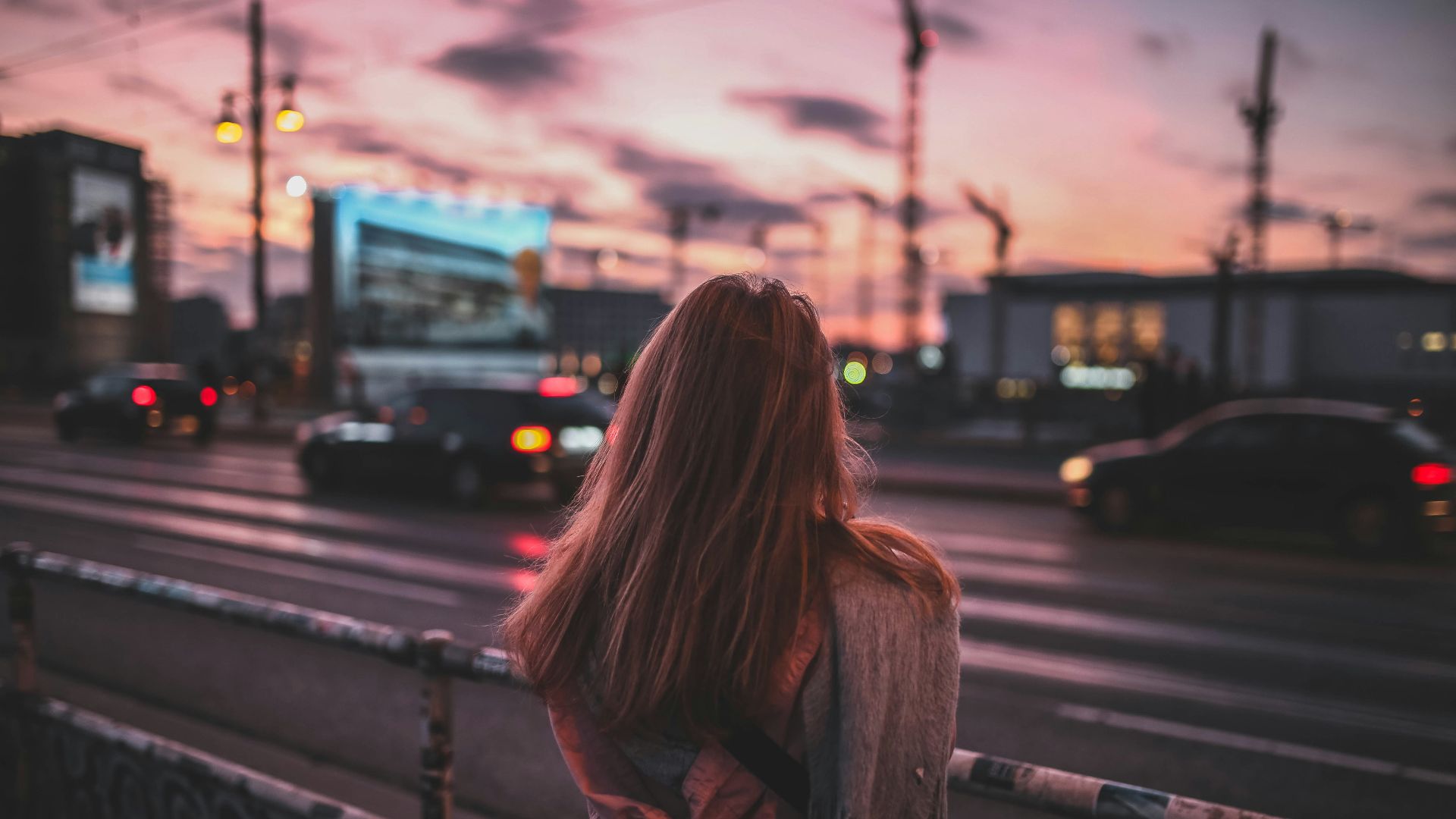 woman standing on rail facing road at dusk