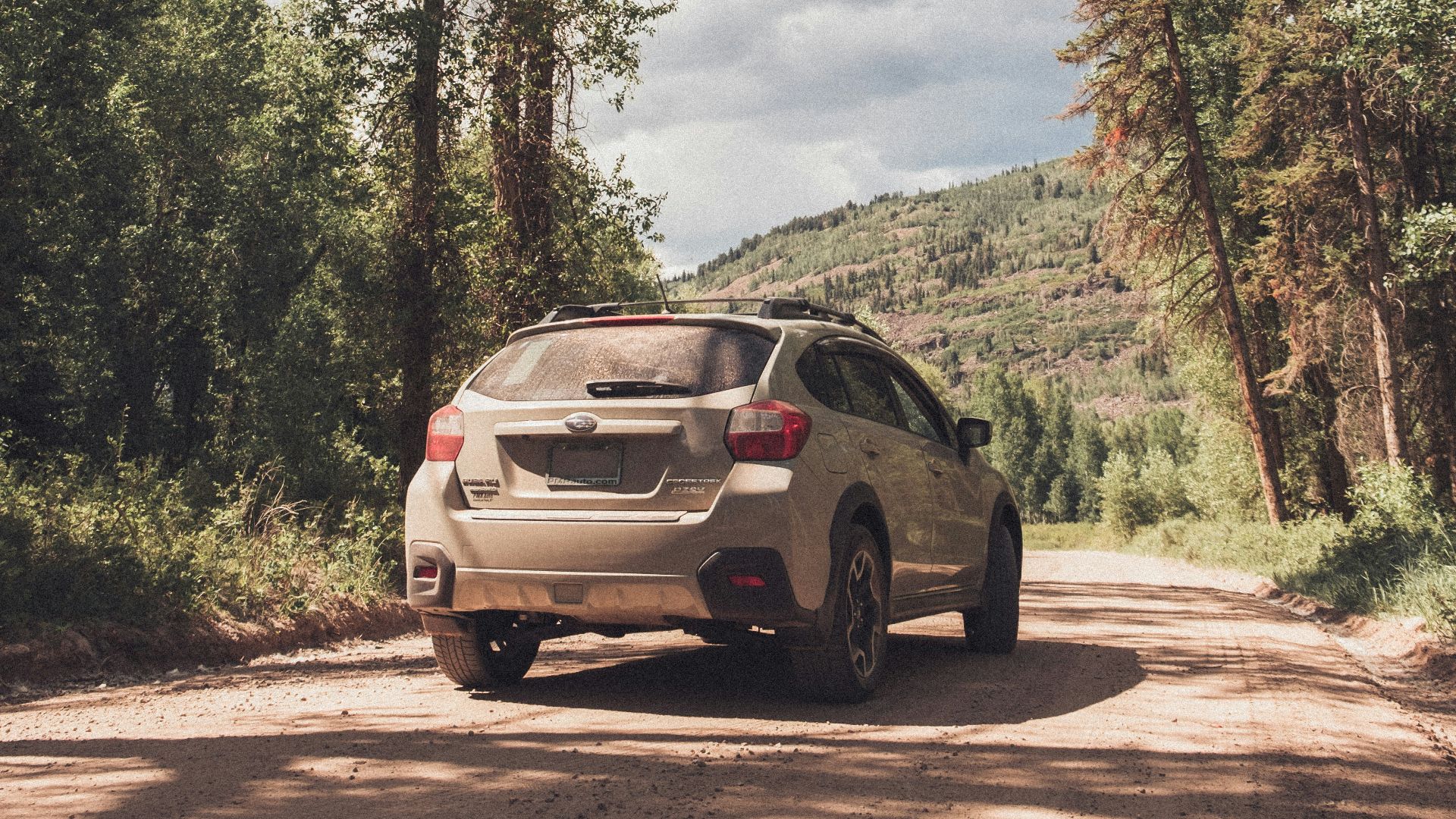 a white car driving down a dirt road next to a forest