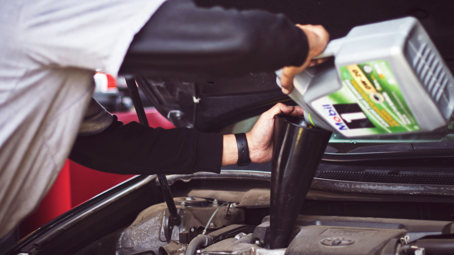 man refilling motor oil on car engine bay