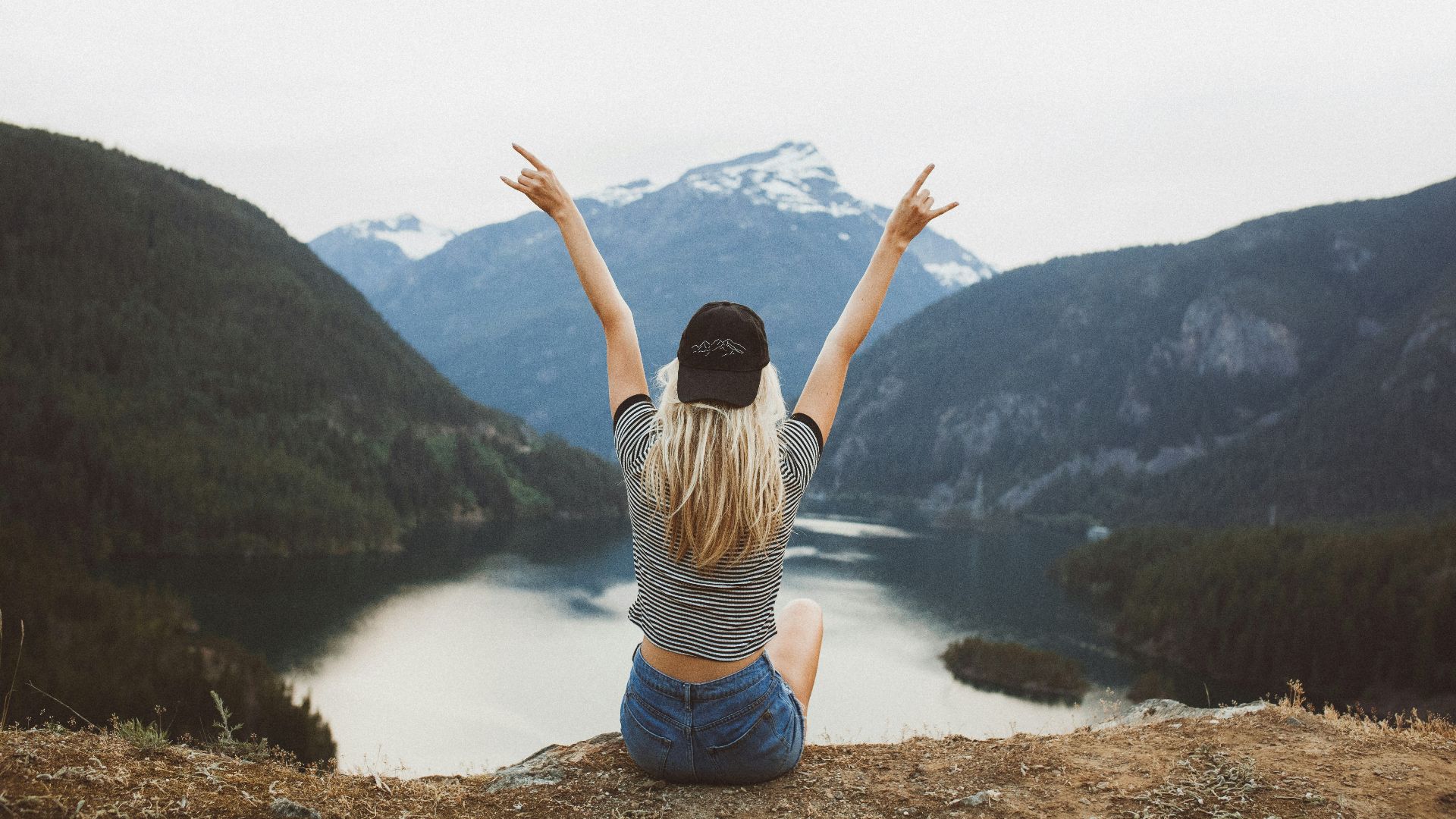 woman sitting on cliff raising both hands