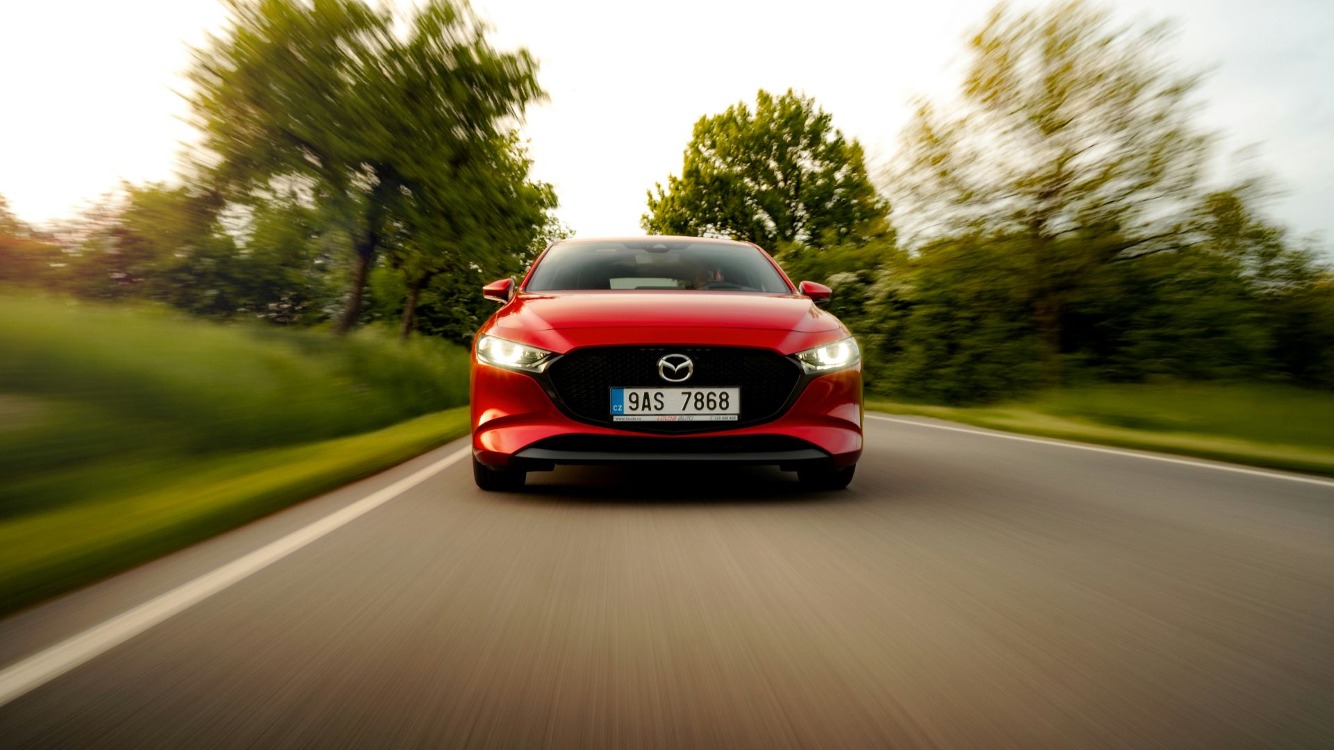 a red car driving down a road with trees in the background