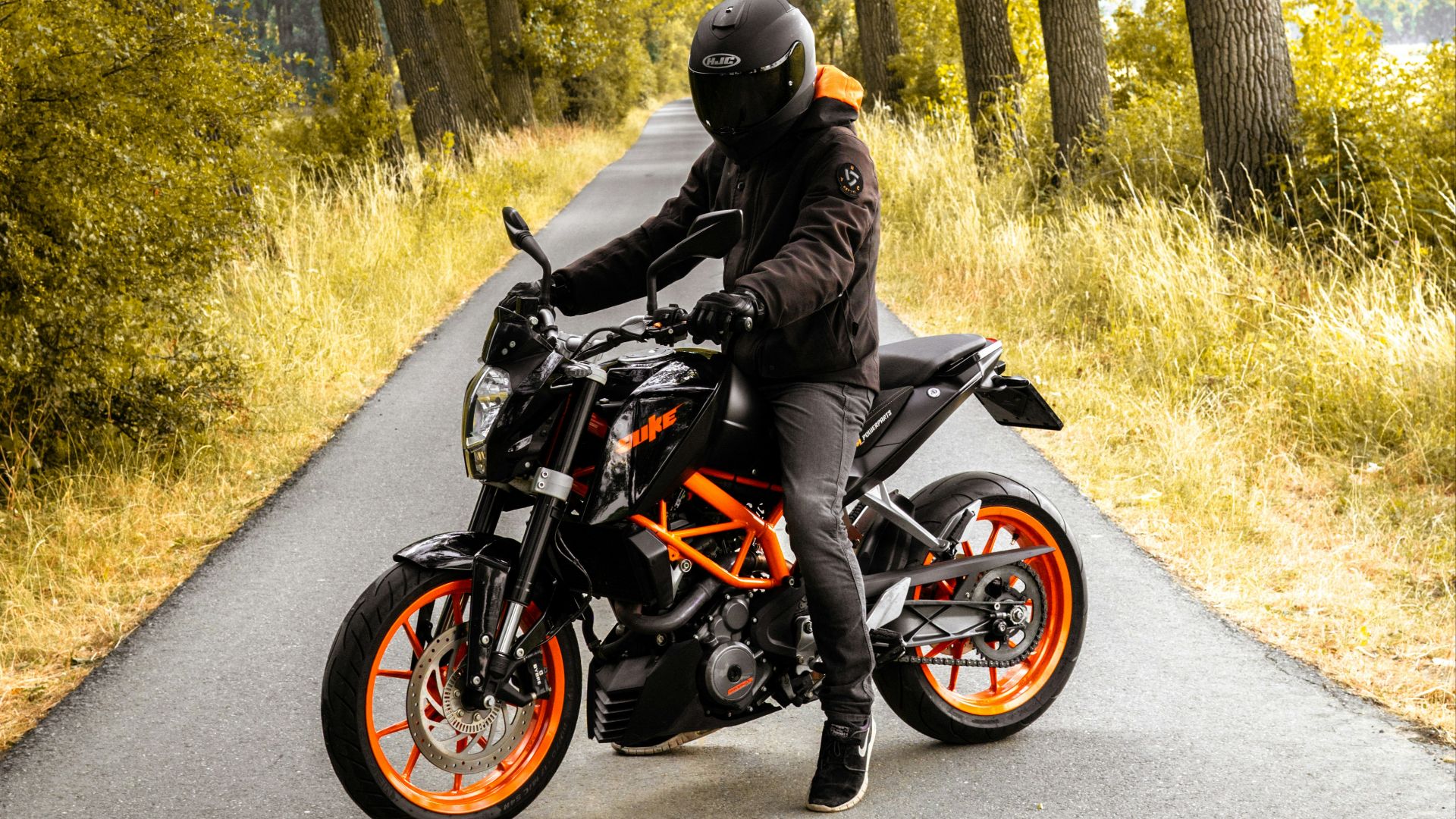 man riding black and orange motorcycle beside trees