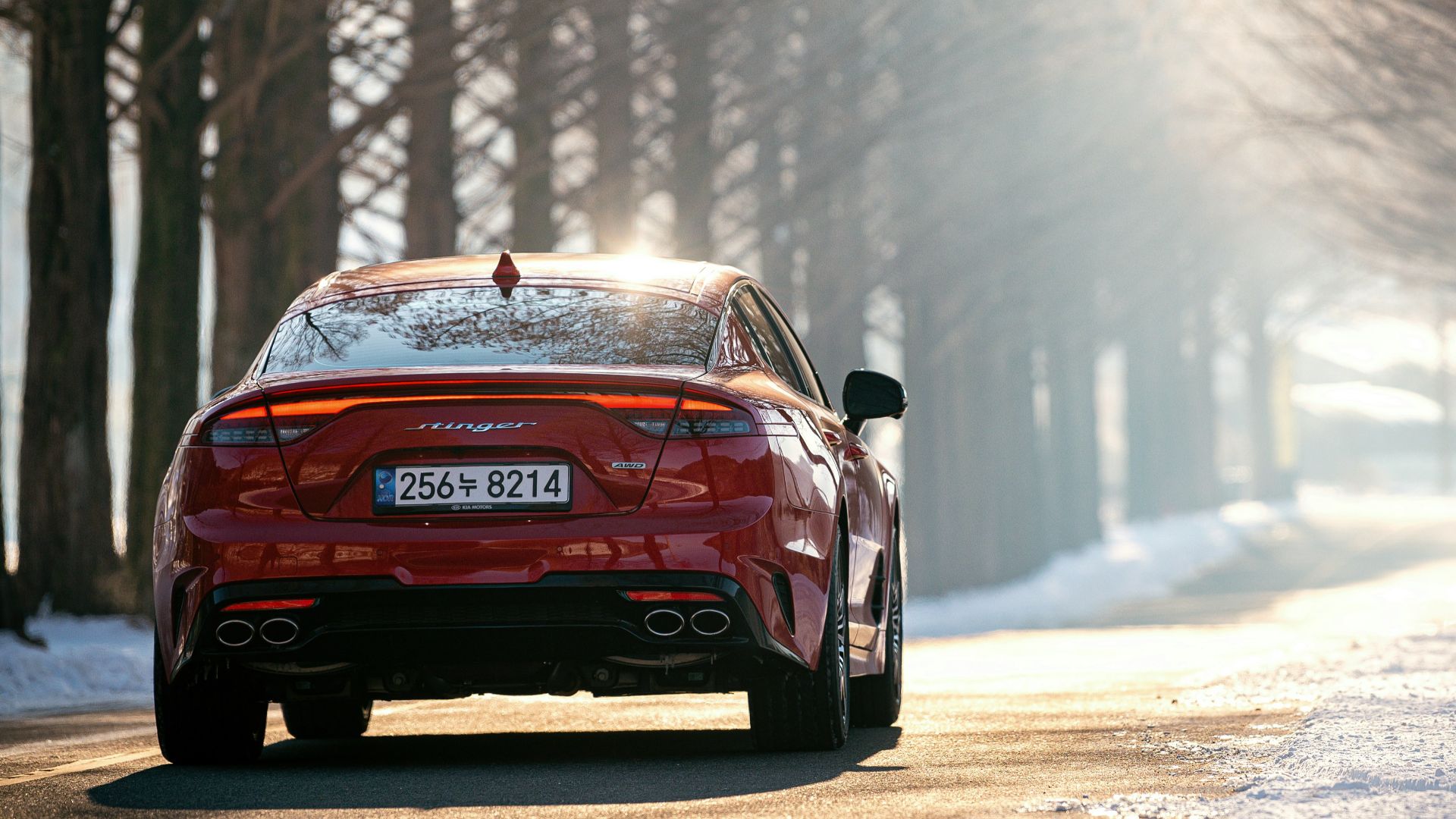 a red car driving on a road with snow on the side