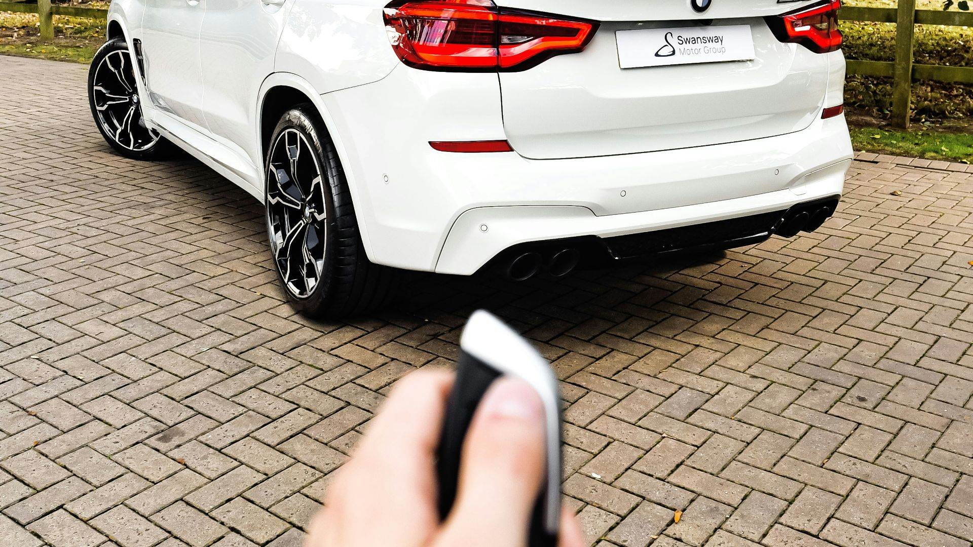 a hand holding a phone in front of a white car