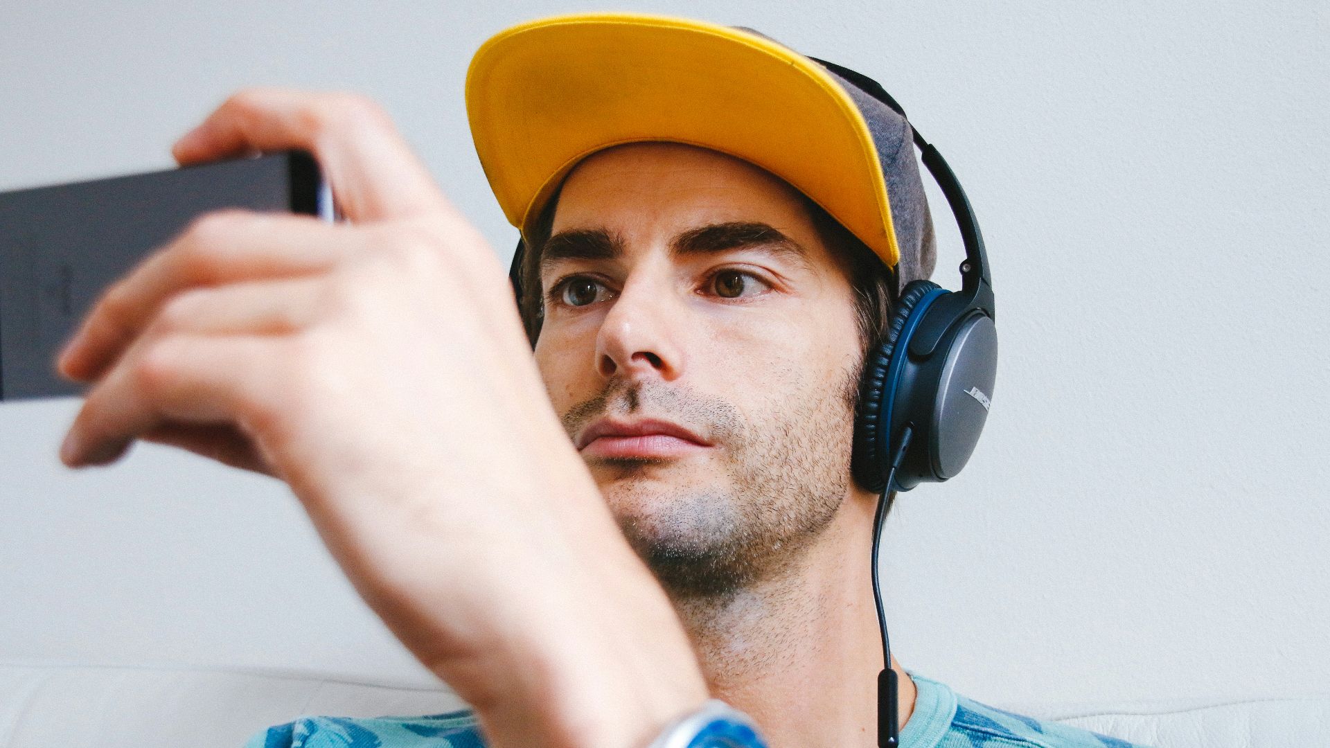man wearing black corded headphones while holding phone