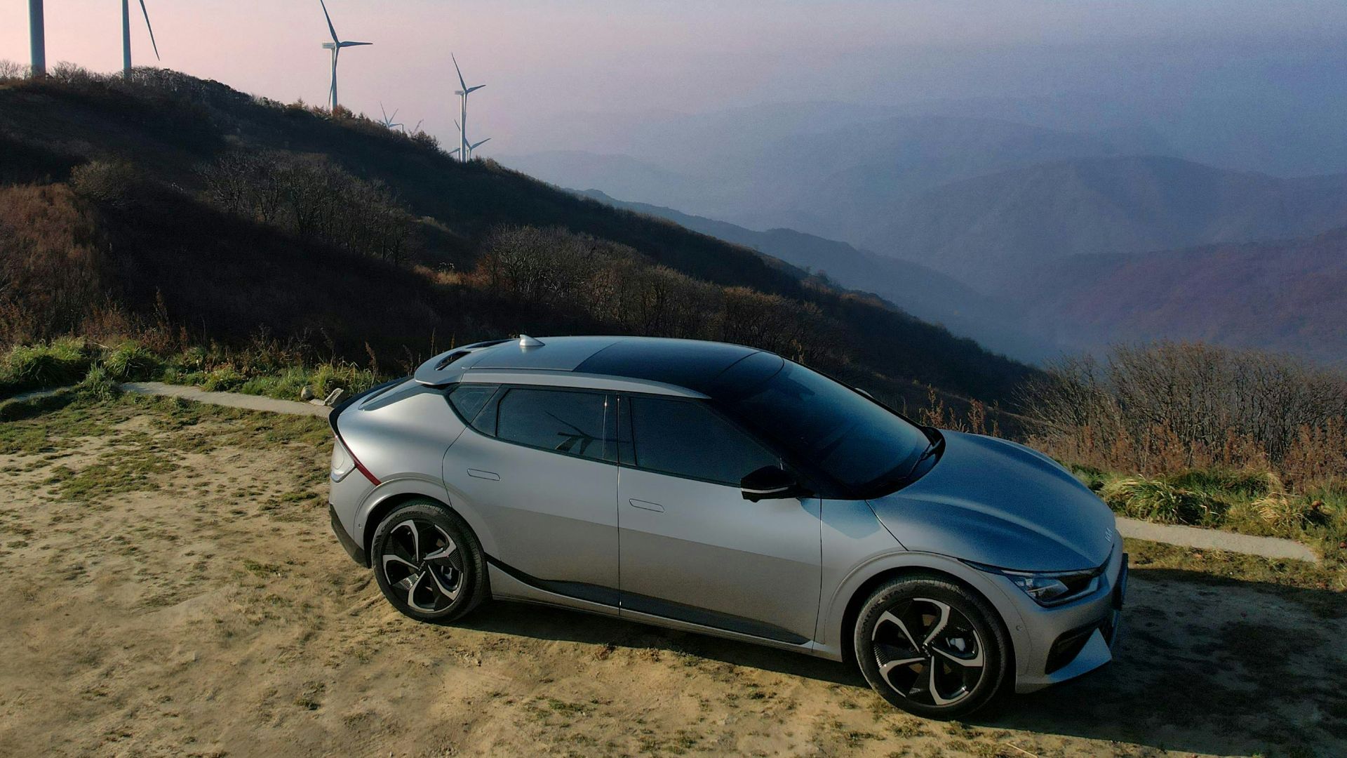 a car parked on a dirt road next to wind turbines